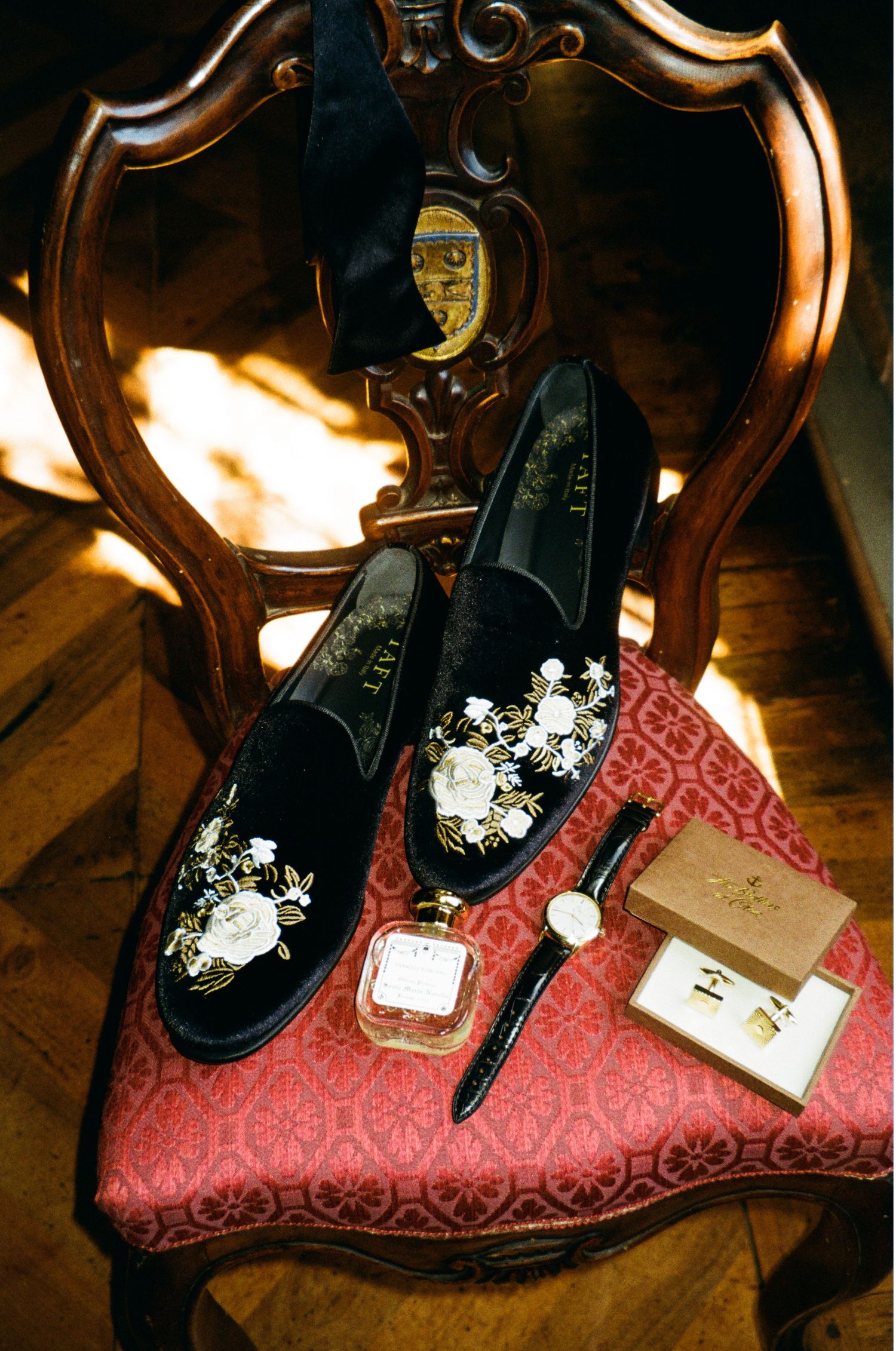 Elegant black velvet embroidered wedding loafers displayed on an antique chair with a watch and cufflinks.