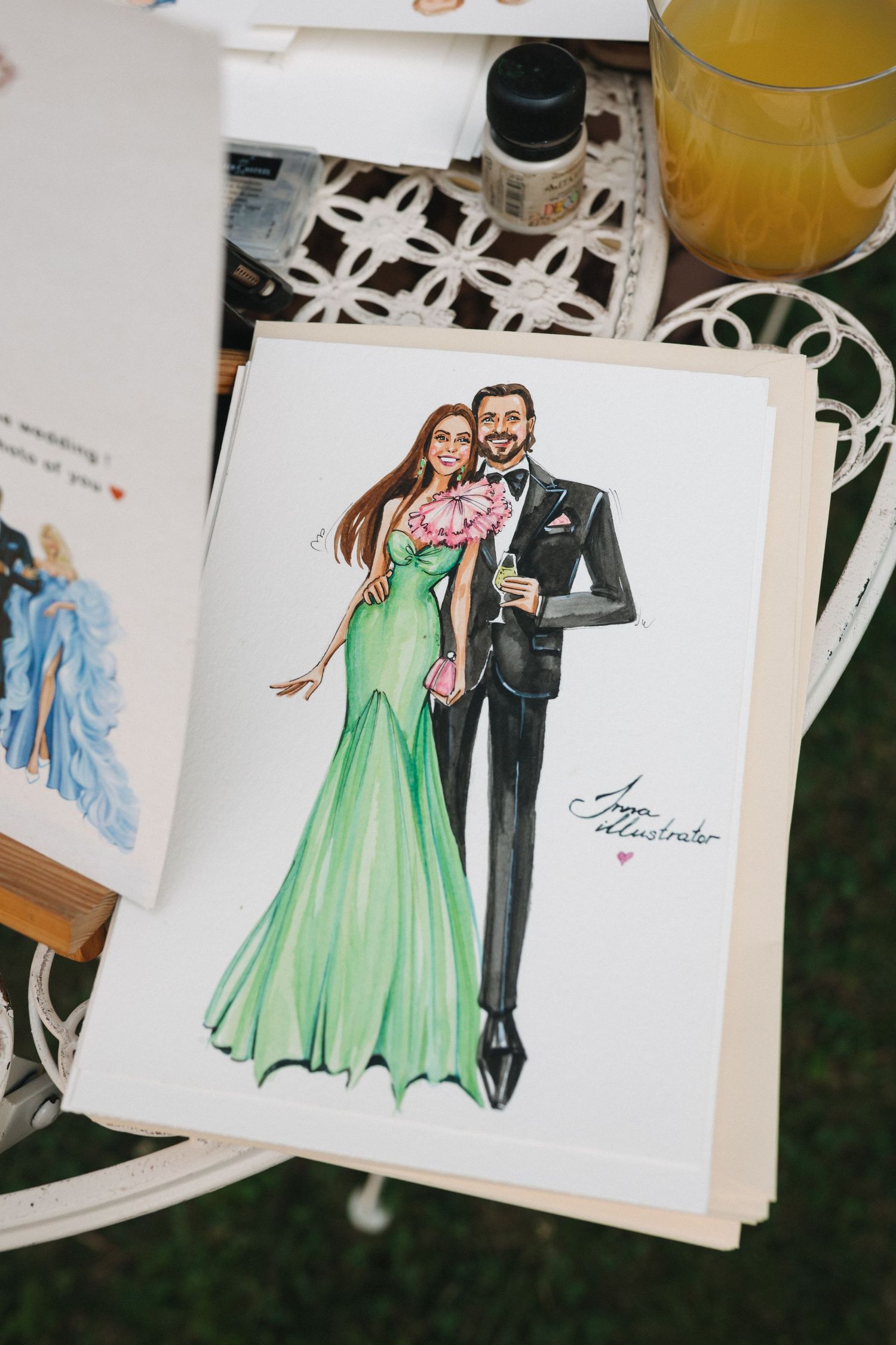 Illustrated wedding portrait of a couple, woman in green gown, man in black tuxedo, displayed on a white table.