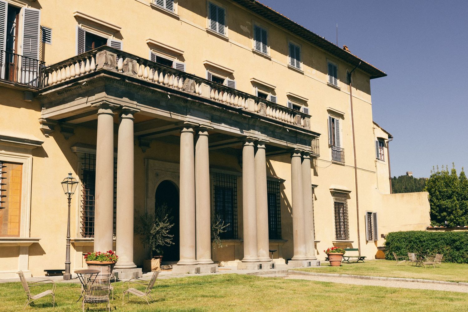 Elegant Italian villa with classical columns, balcony, and manicured lawn under soft natural light.