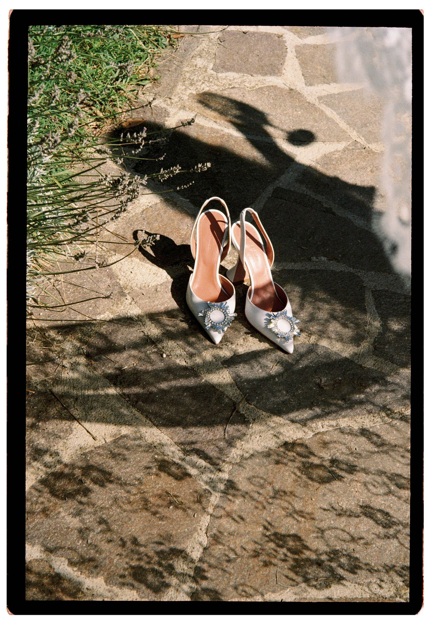 Elegant silver slingback heels with jeweled brooches placed on stone pavement with decorative shadows.