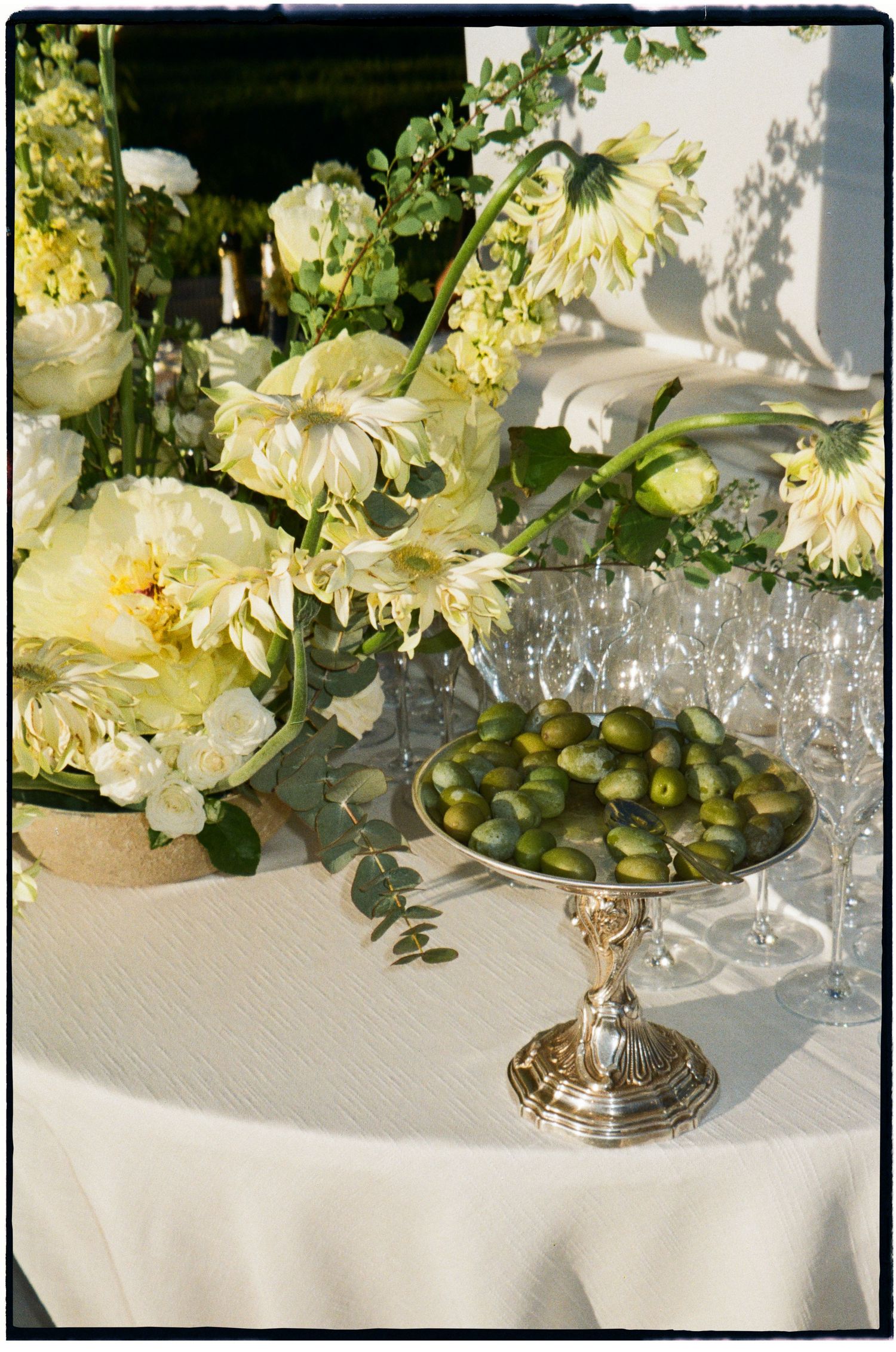 An elegant wedding table display featuring cream peonies, white flowers, and a silver pedestal dish of green olives.