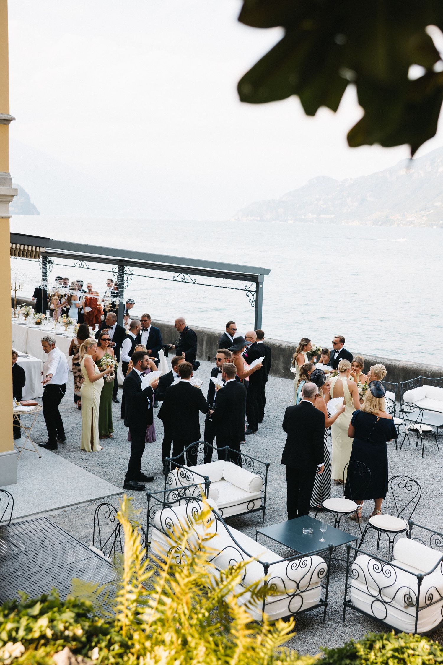 Elegant outdoor wedding reception on a lakeside terrace in Italy with guests in formal attire enjoying cocktail hour.