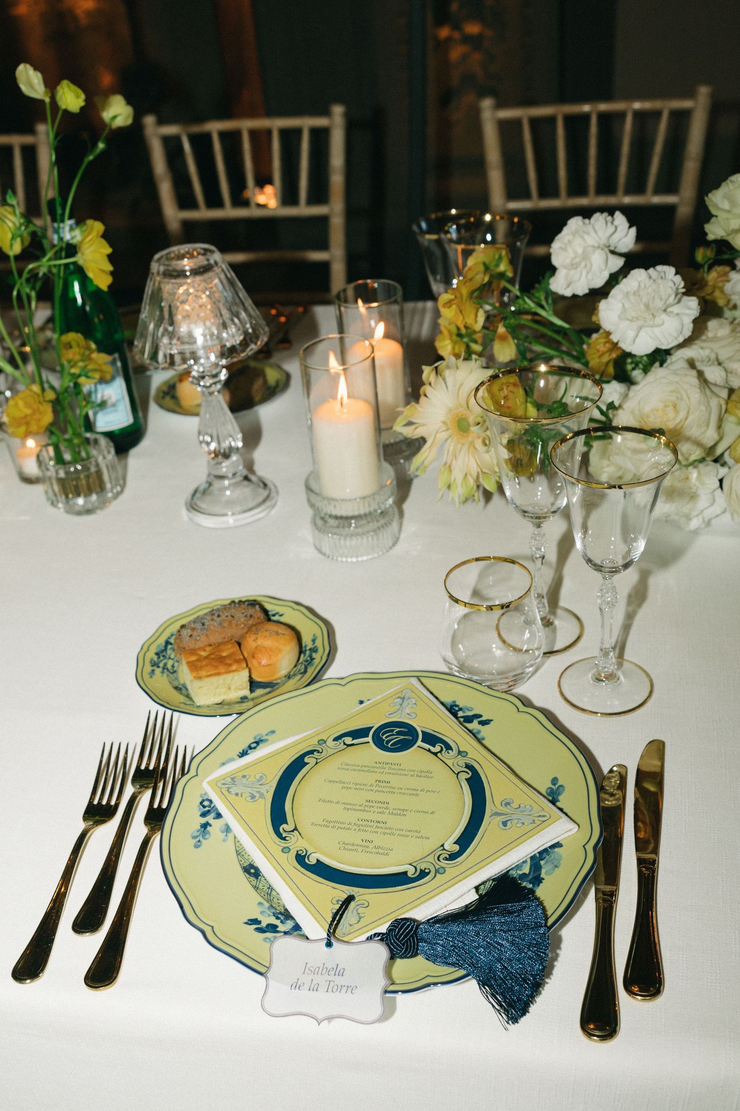 Elegant wedding reception place setting with green plates, gold accents, candles, and floral centerpiece.