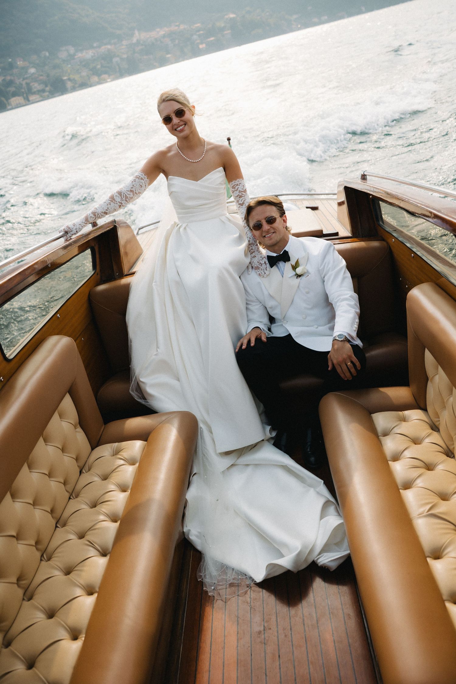 Bride and groom in wedding attire relaxing on a luxury wooden boat on Lake Como, Italy.