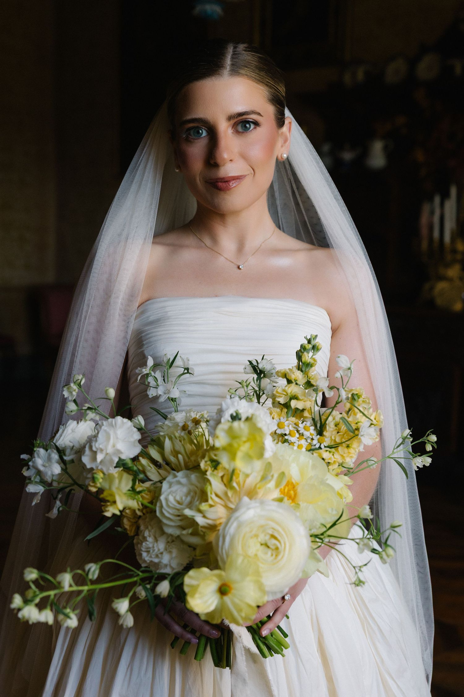 Bride in strapless white gown and veil holding lush yellow and white floral bouquet on her wedding day.