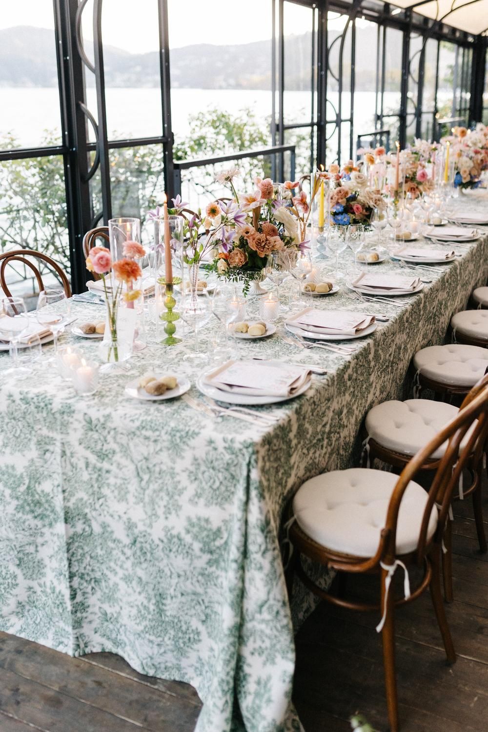 Elegant wedding reception table with green toile tablecloth, colorful floral centerpieces and candles overlooking lake view.