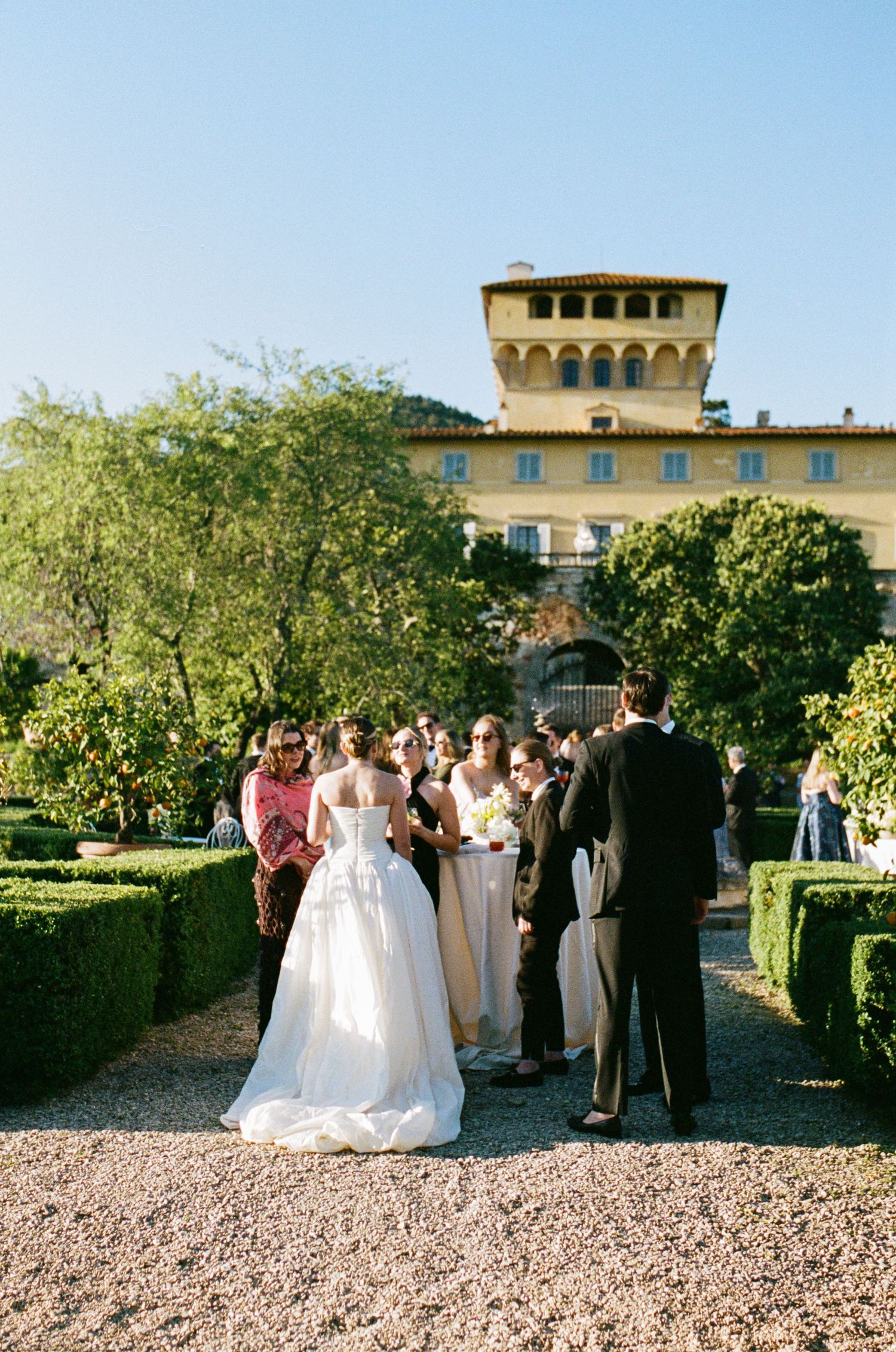 Bride in white ball gown with guests at outdoor wedding ceremony in elegant Italian villa garden.