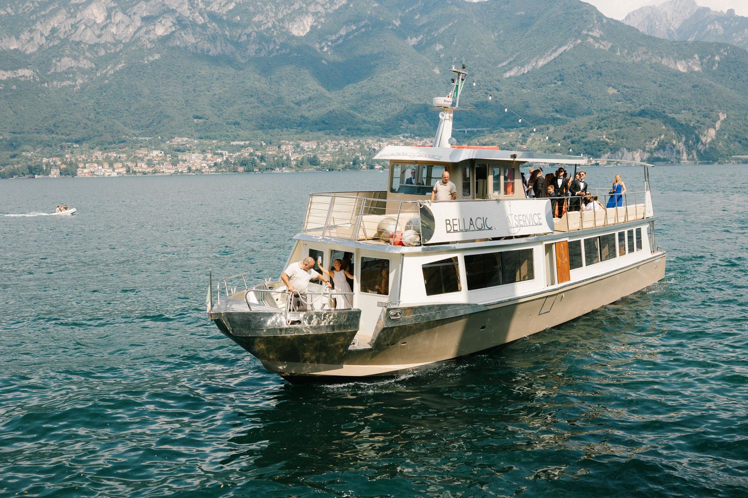 A white passenger ferry boat cruising on a blue alpine lake surrounded by mountains with tourists on deck.