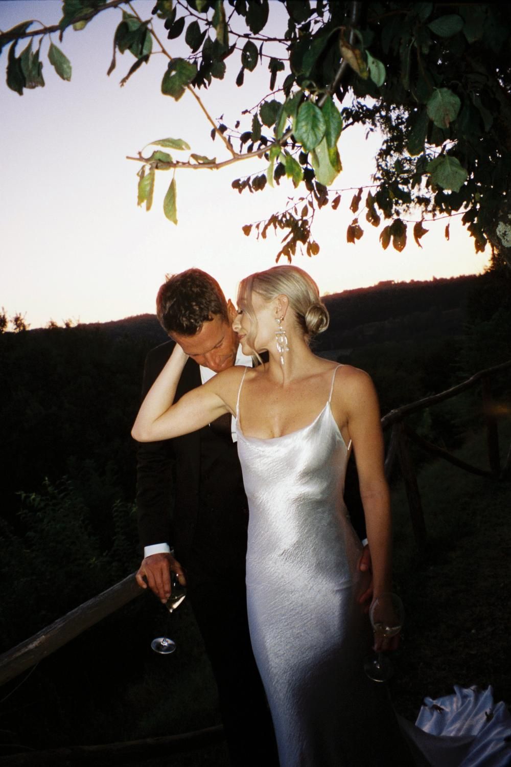 Couple in formal wedding attire sharing intimate moment at sunset with scenic landscape view.