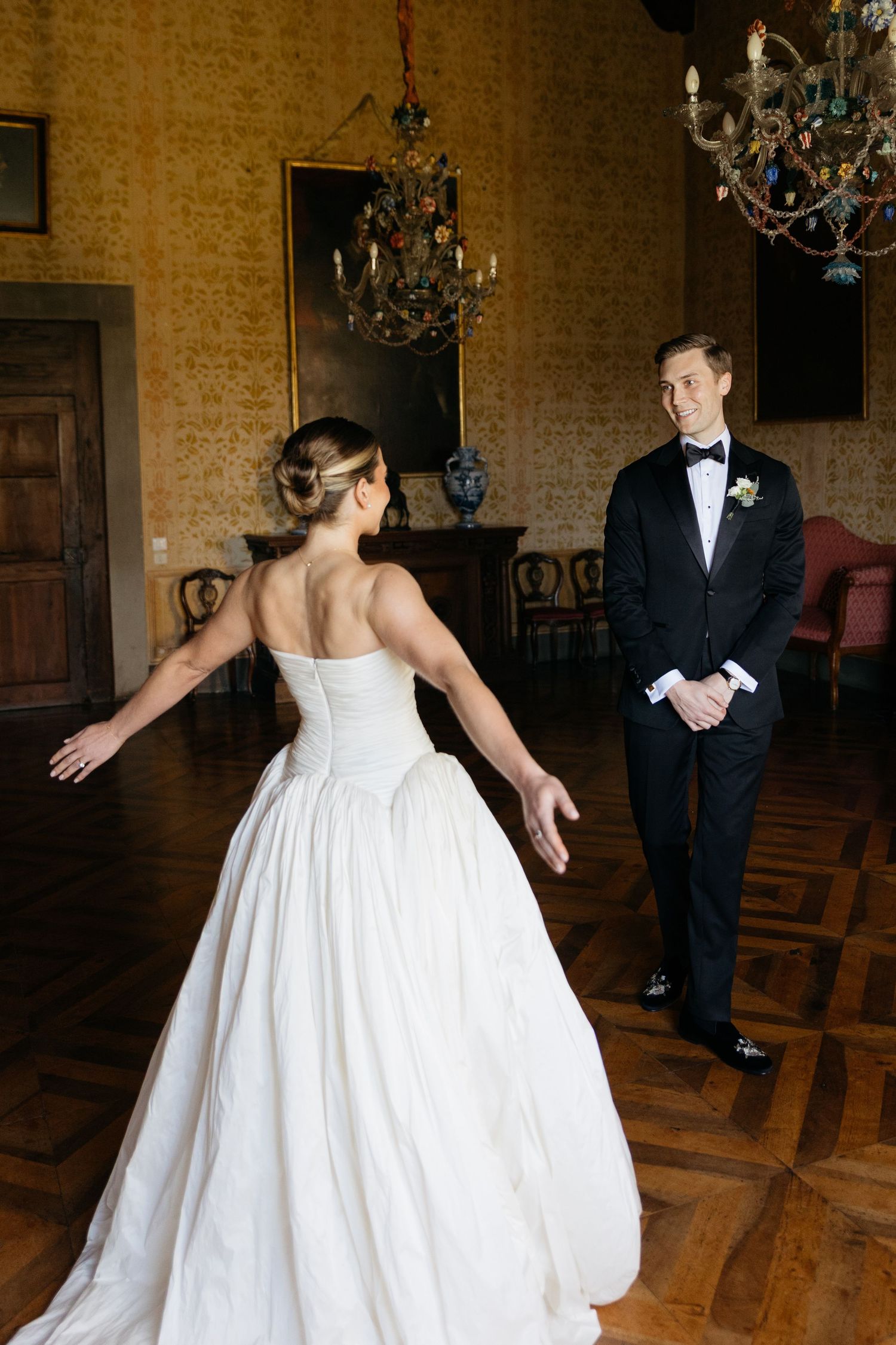 Bride in strapless white ball gown turns to reveal herself to groom in black tuxedo during wedding first look.