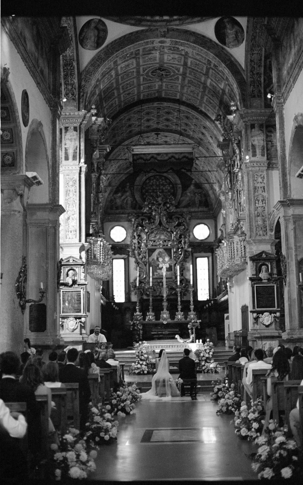 Black and white aerial view of a bride and groom at the altar of an ornate historic church during wedding ceremony.