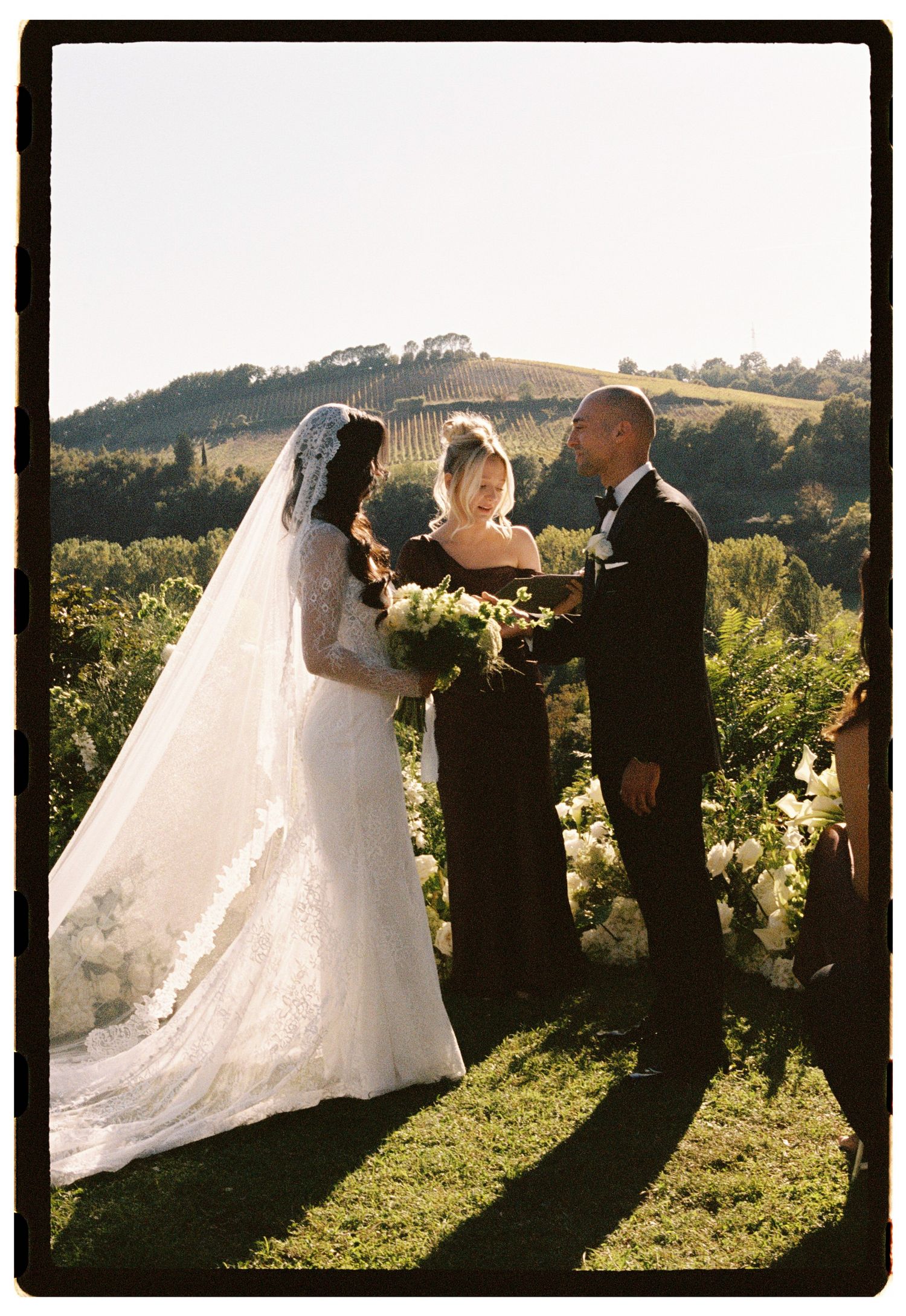 Bride and groom exchange vows at outdoor vineyard wedding ceremony with rolling hills backdrop.