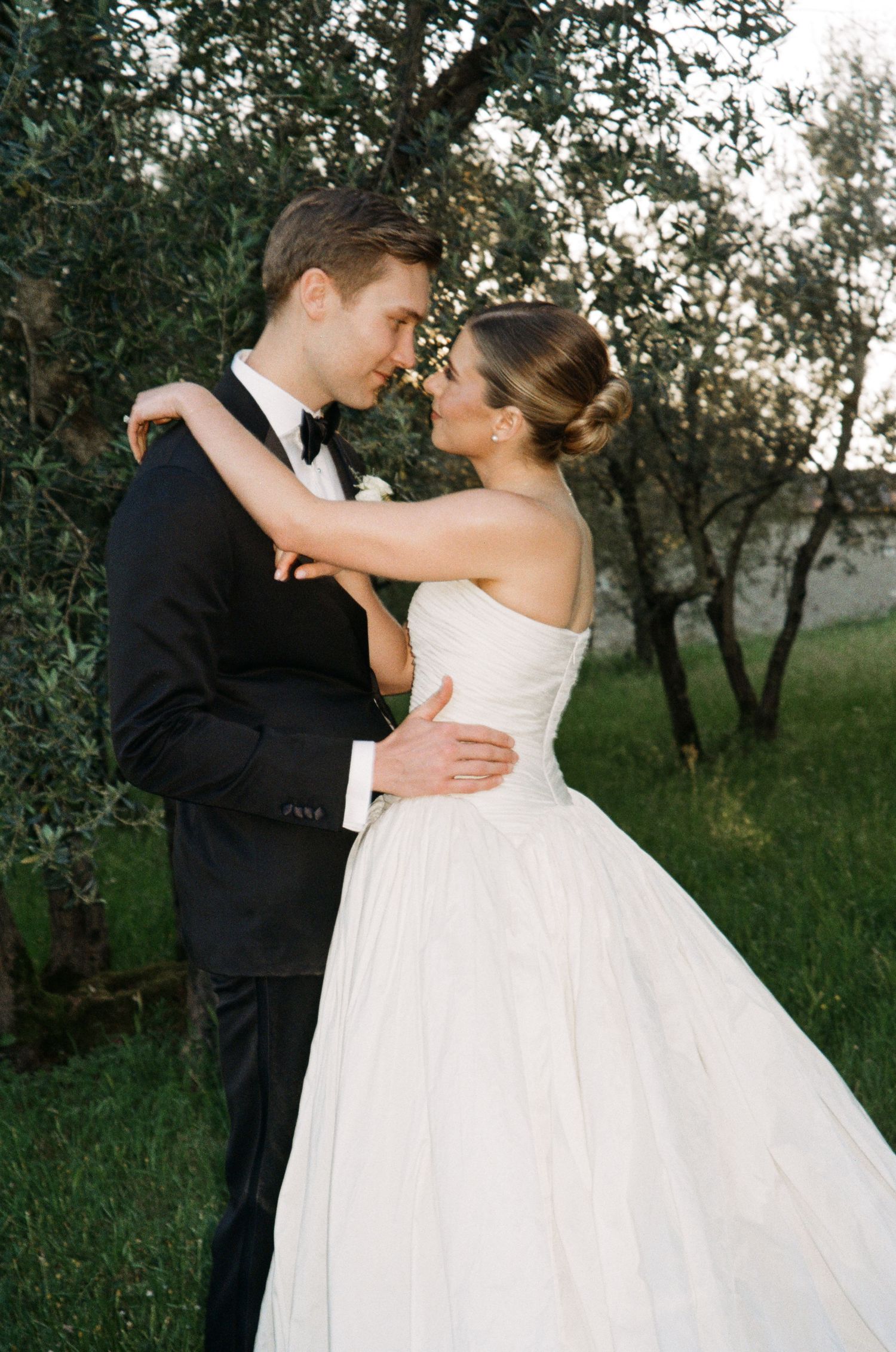 Bride and groom share romantic moment in garden, she wears strapless ball gown, he wears black tuxedo.