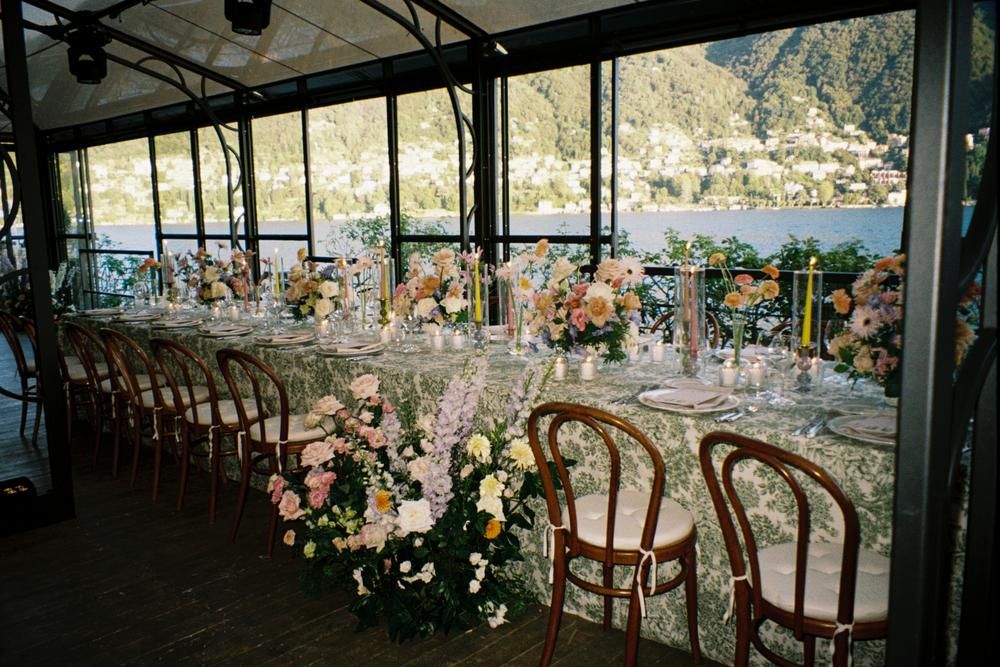 Elegant lakeside wedding reception with floral centerpieces, patterned tablecloths, and mountain views.