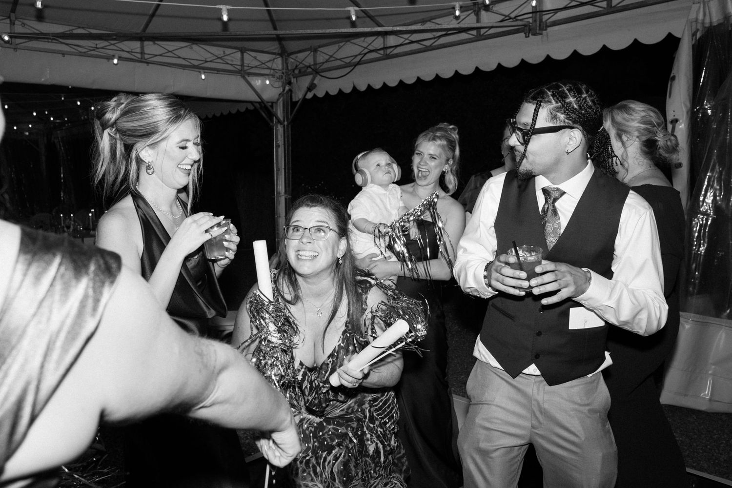 Black and white photo of guests laughing and celebrating at a wedding reception under a tent.