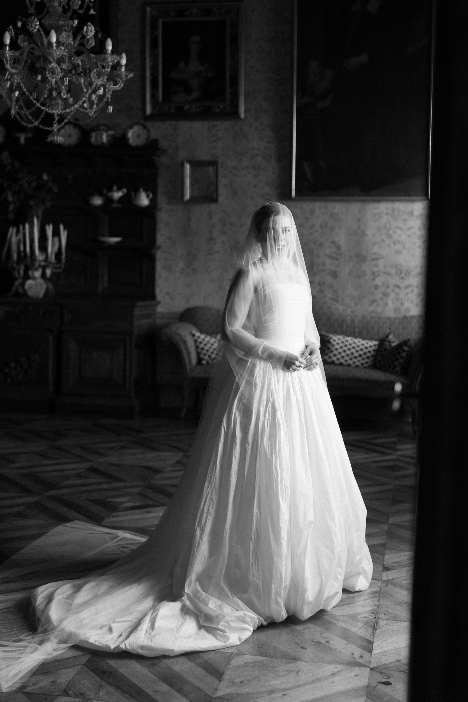 Black and white portrait of bride in full veil and flowing gown in grand interior.