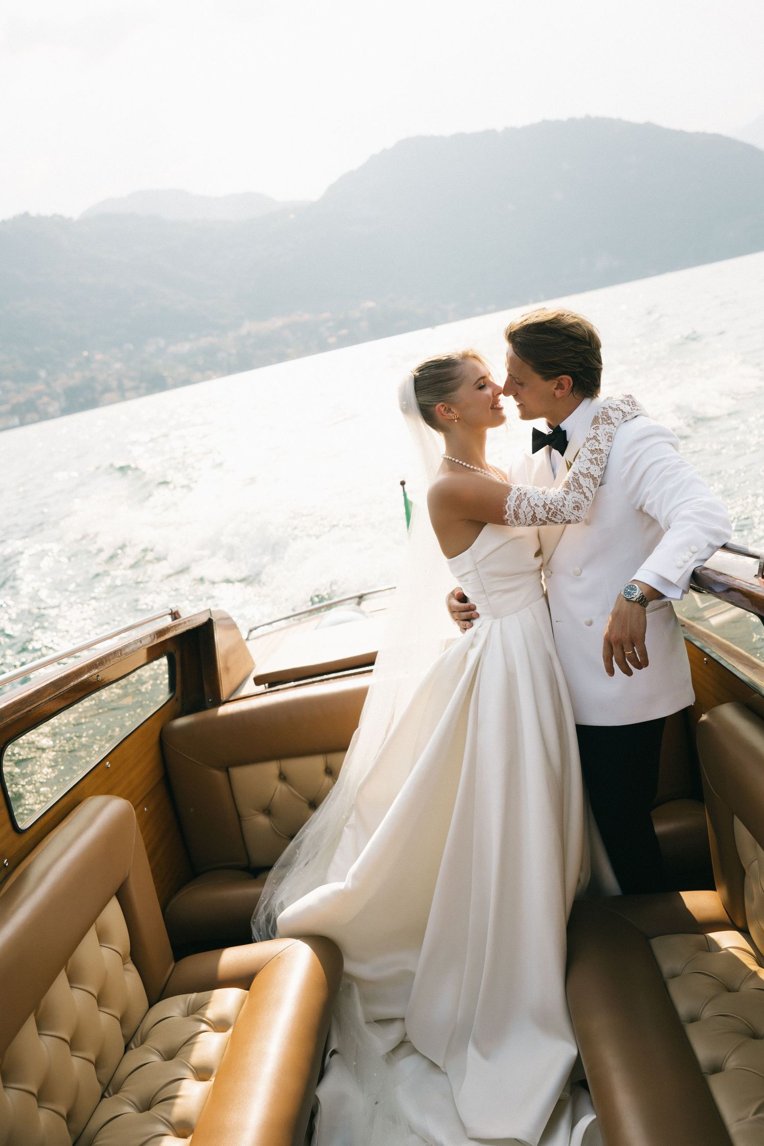 Bride and groom share a romantic moment on a luxury boat with mountain lake views on their wedding day.