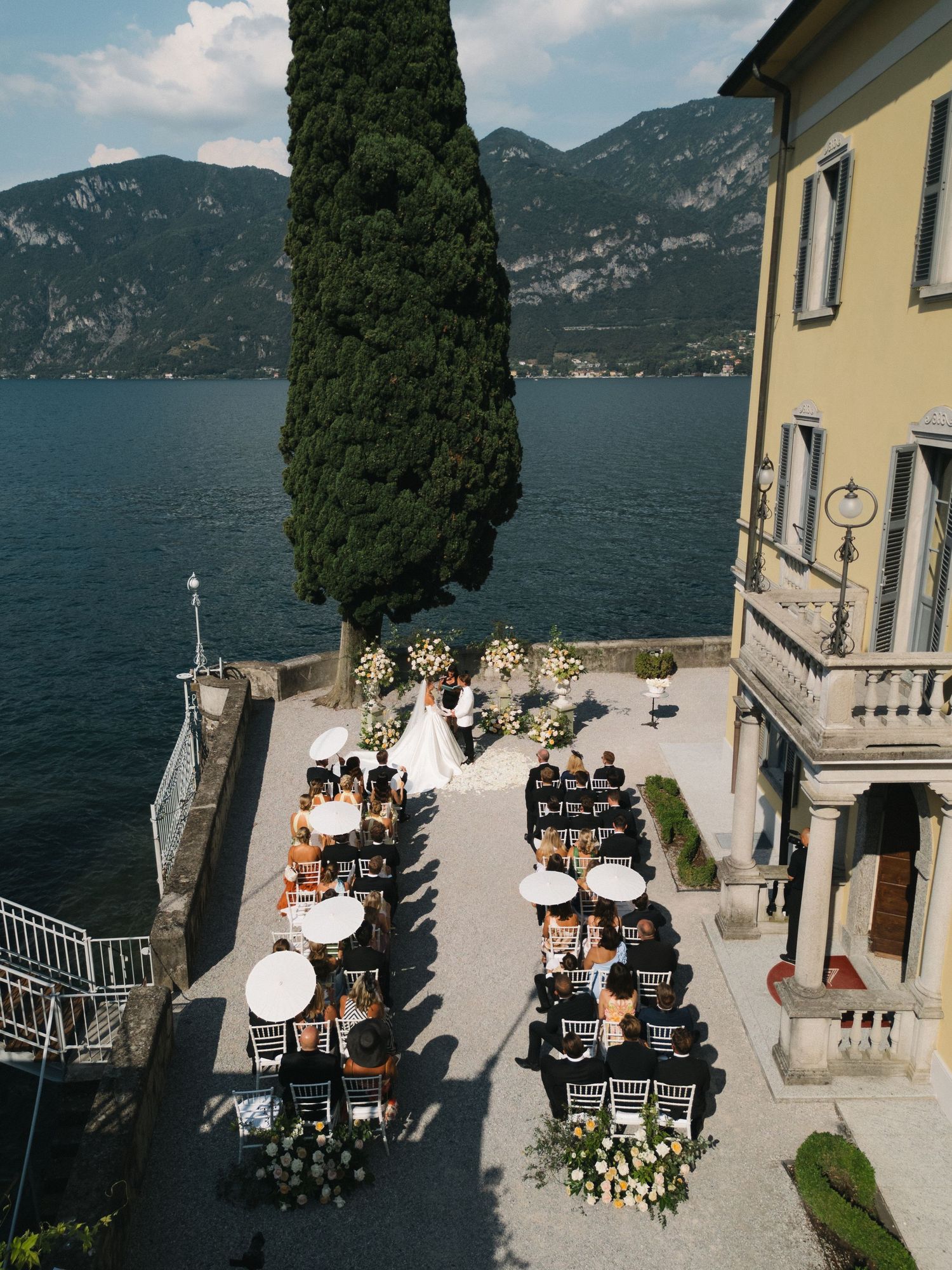 Aerial view of an elegant lakeside wedding ceremony at Villa del Balbianello, Lake Como, Italy, with guests seated outdoors.