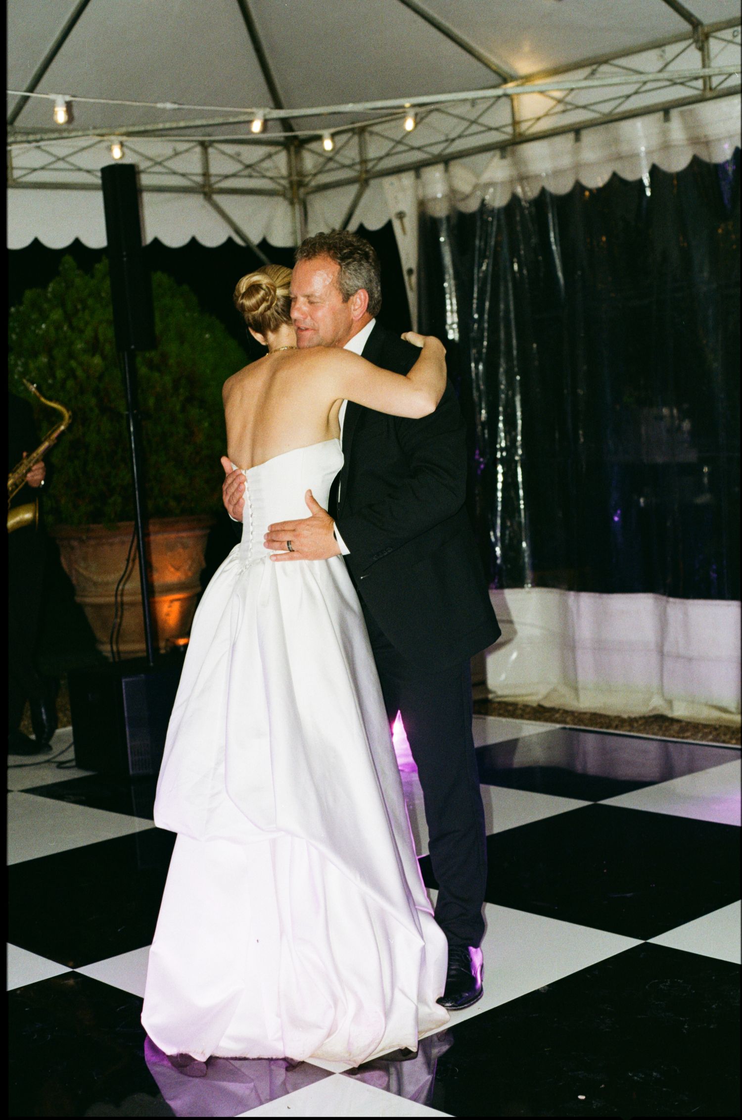 Bride and groom share their first dance on a black and white checkered floor under a white tent at their wedding reception.