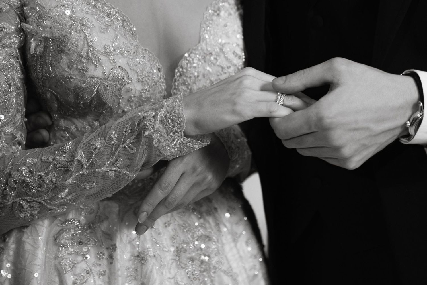 Black and white close-up of bride and groom exchanging wedding rings during ceremony.