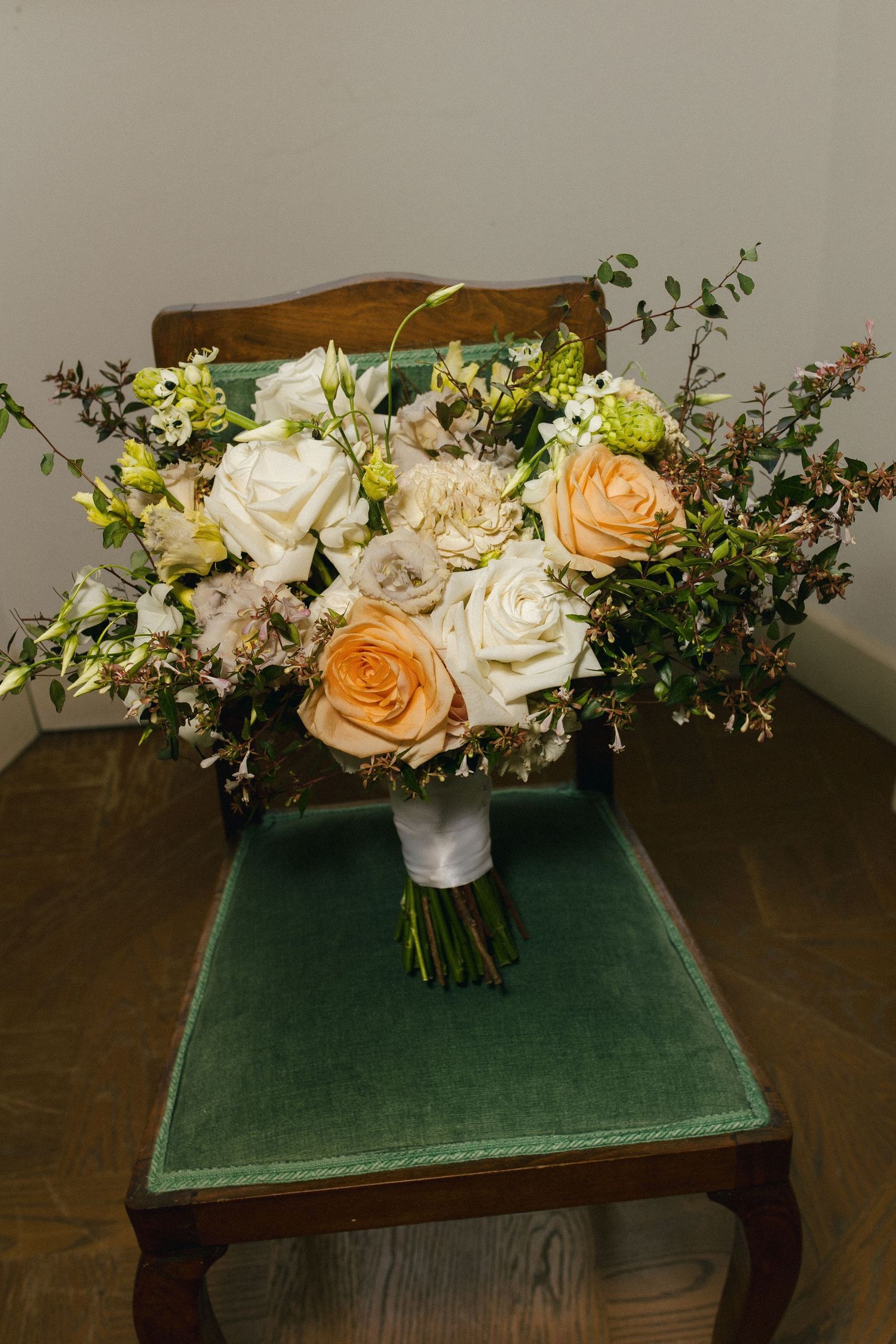 Elegant bridal bouquet with peach and white roses on a green velvet chair.