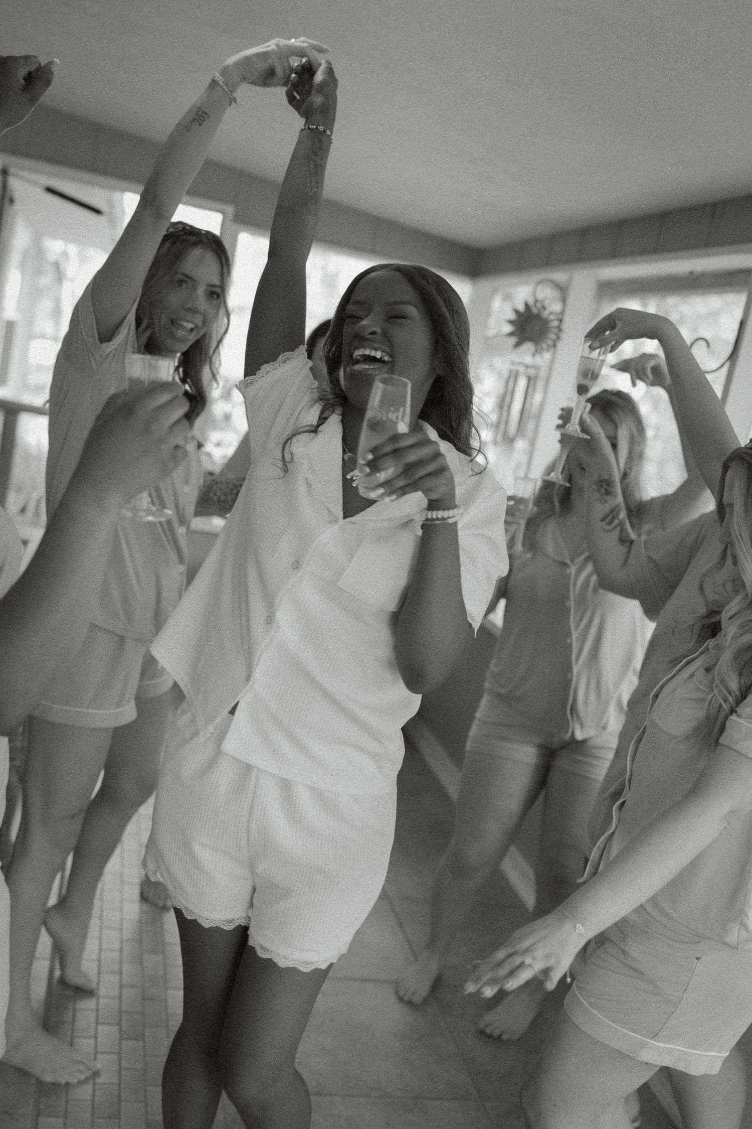 Women in white robes dancing and celebrating at a bachelorette party in black and white photo.