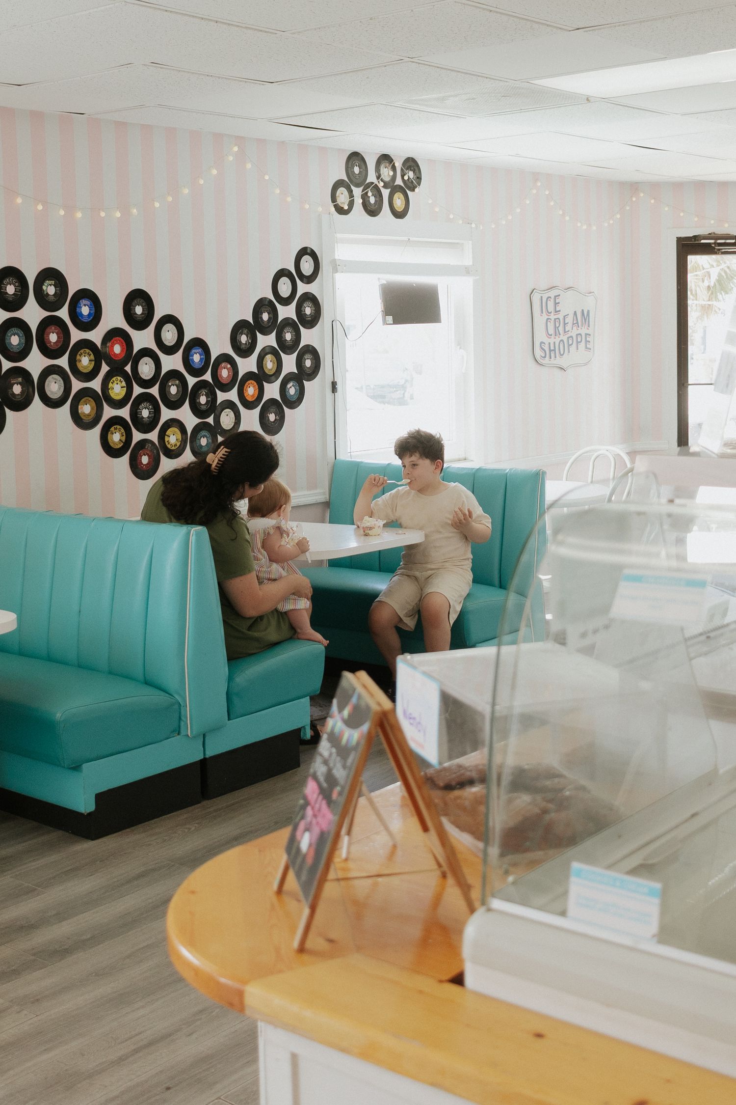 Family enjoying ice cream at a retro shoppe with teal booths and vinyl records on striped walls.