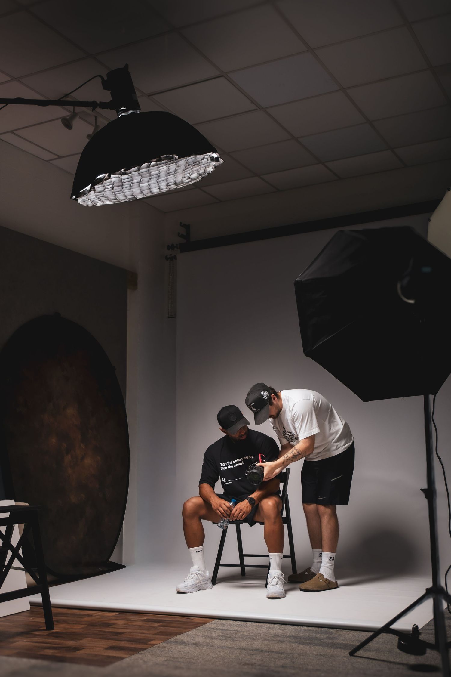 Photographer adjusting camera settings for seated subject in professional photography studio with softbox lighting equipment.