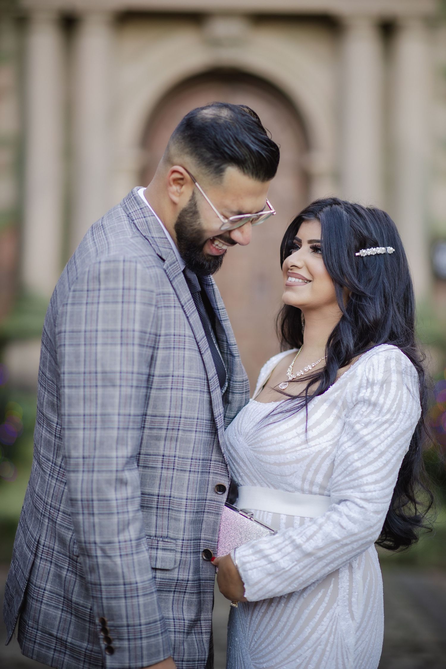 A couple in wedding attire sharing a romantic moment outdoors, the bride smiling beautifully at her groom.