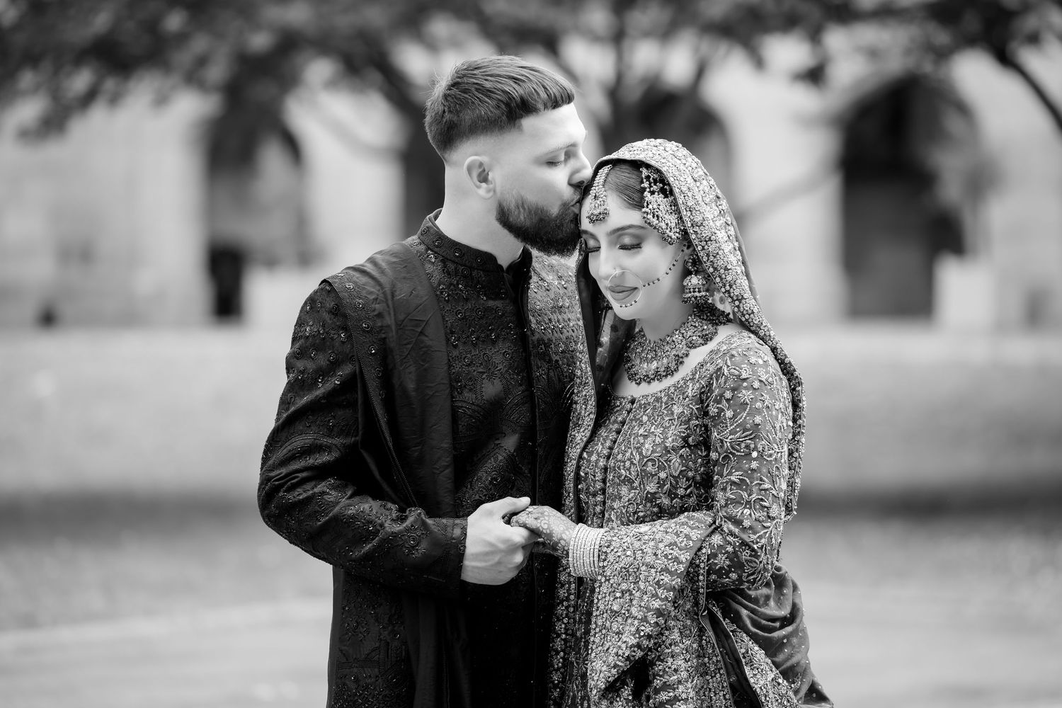Black and white photo of a South Asian couple in traditional wedding attire, bride in embroidered dupatta, groom in sherwani.