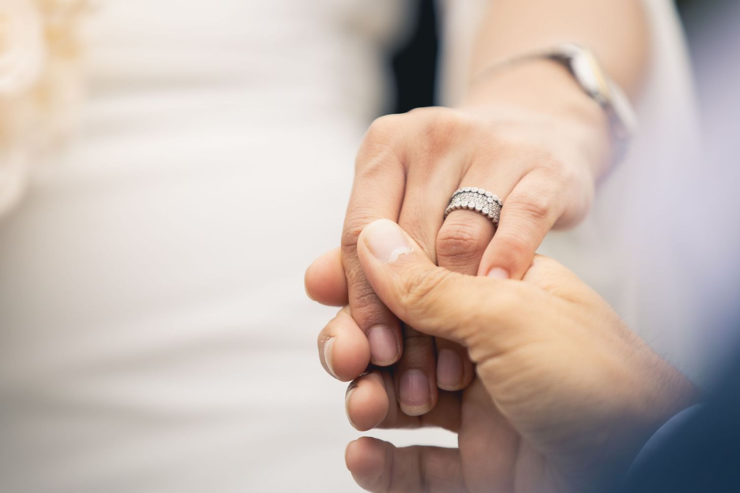 Close-up of bride and groom holding hands, showcasing a sparkling diamond wedding band on the bride's finger.