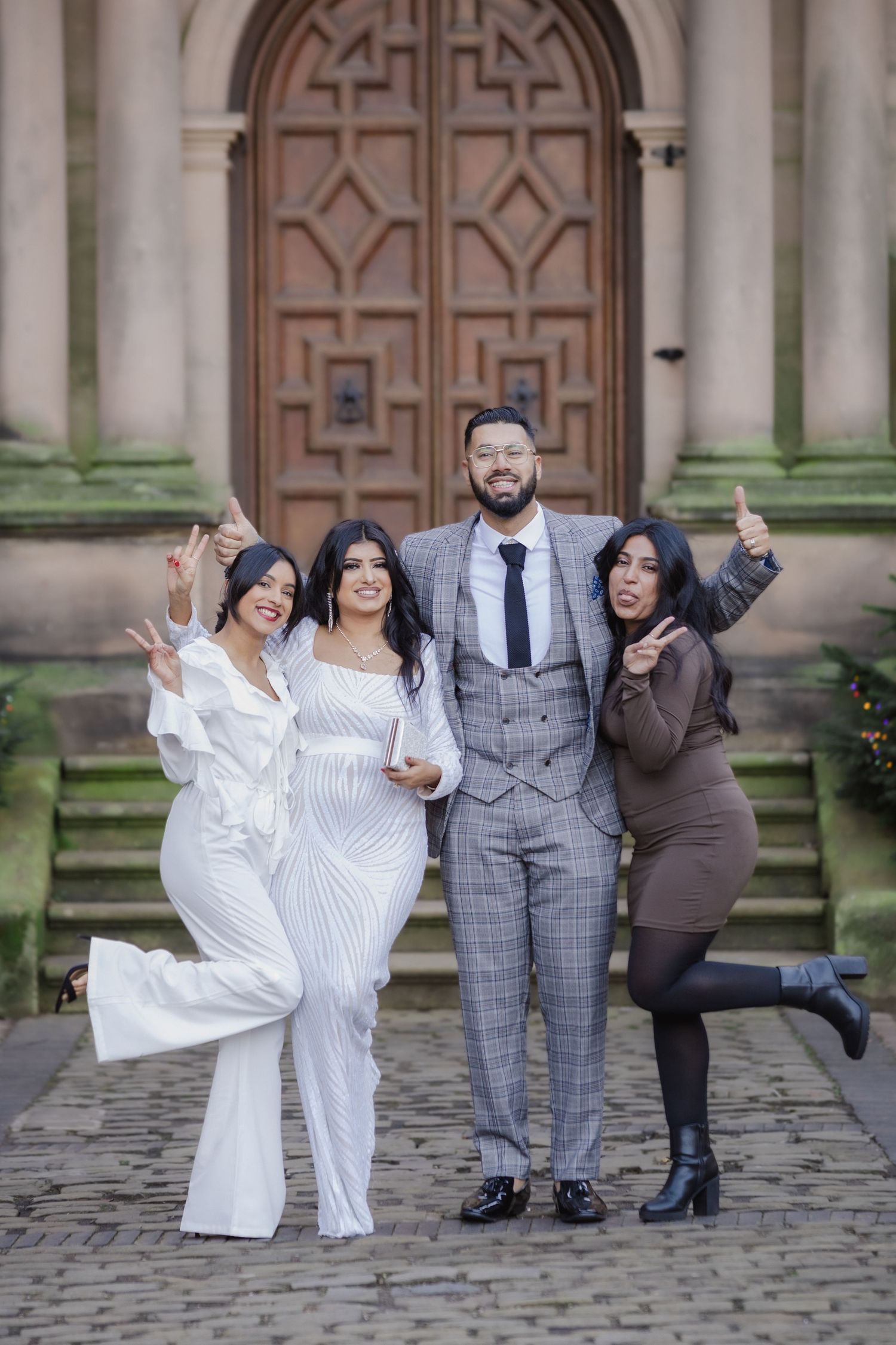 Four elegantly dressed people posing joyfully outside a grand church door, celebrating a wedding occasion.