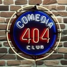 Neon sign for Comedia 404 Club glowing in red and blue on a brick wall background.