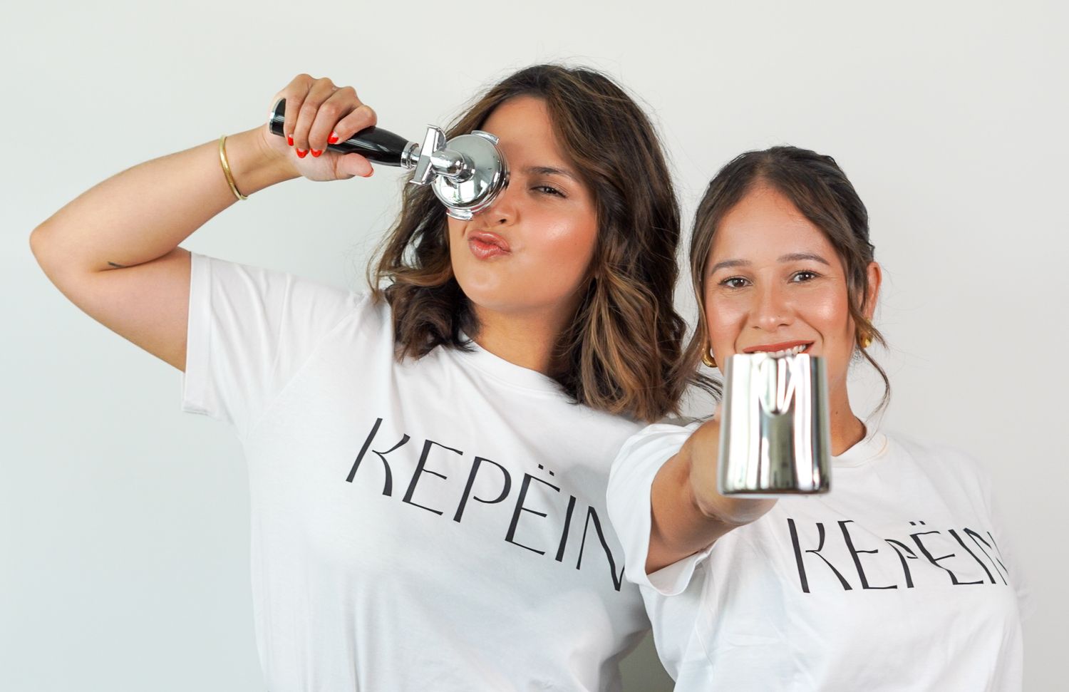 Two women in matching KEPEIN white t-shirts posing playfully with an ice cream scoop and metal cup.