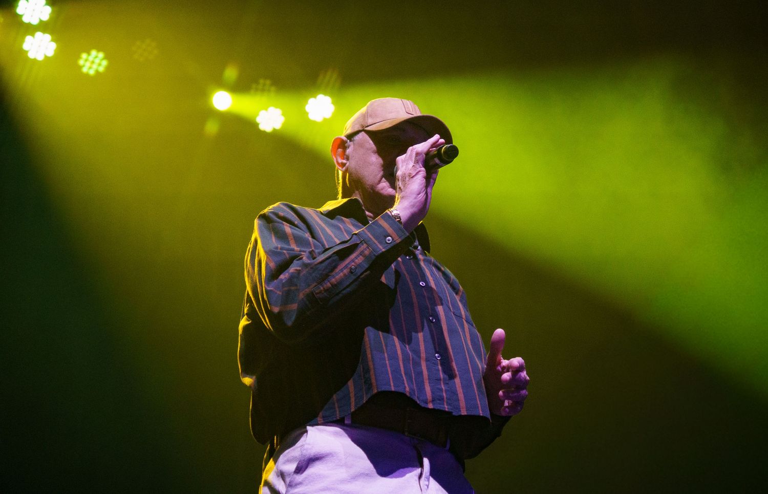 Bald male singer performing on stage under green and yellow stage lights at a live concert.