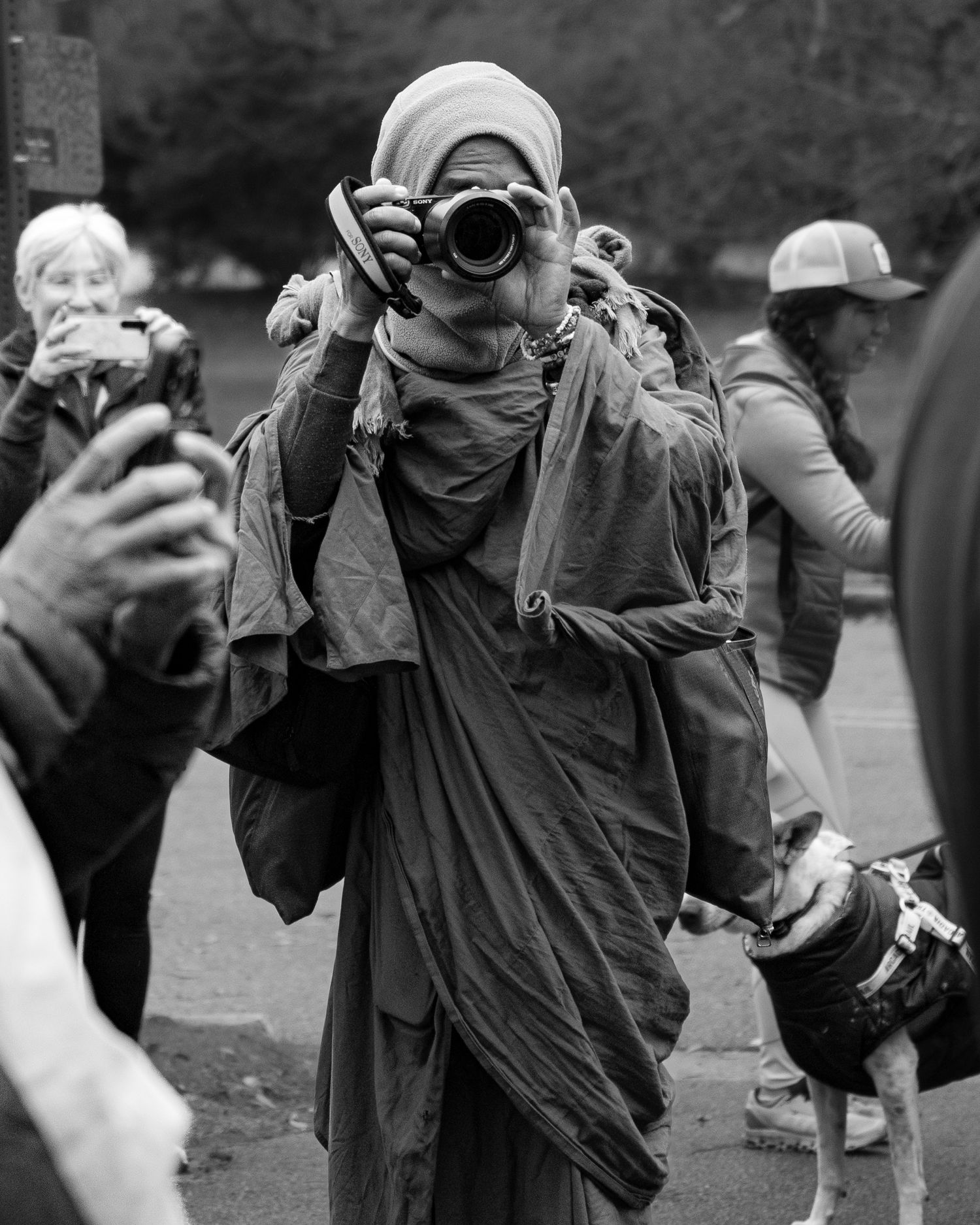 Black and white photo of robed monk taking photos with camera at outdoor gathering.