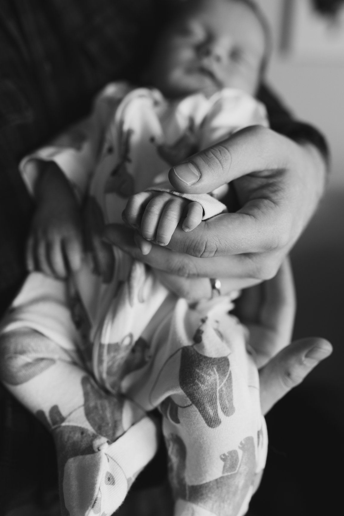 Close-up black and white photo of an adult hand gently holding a sleeping newborn baby's tiny fist.