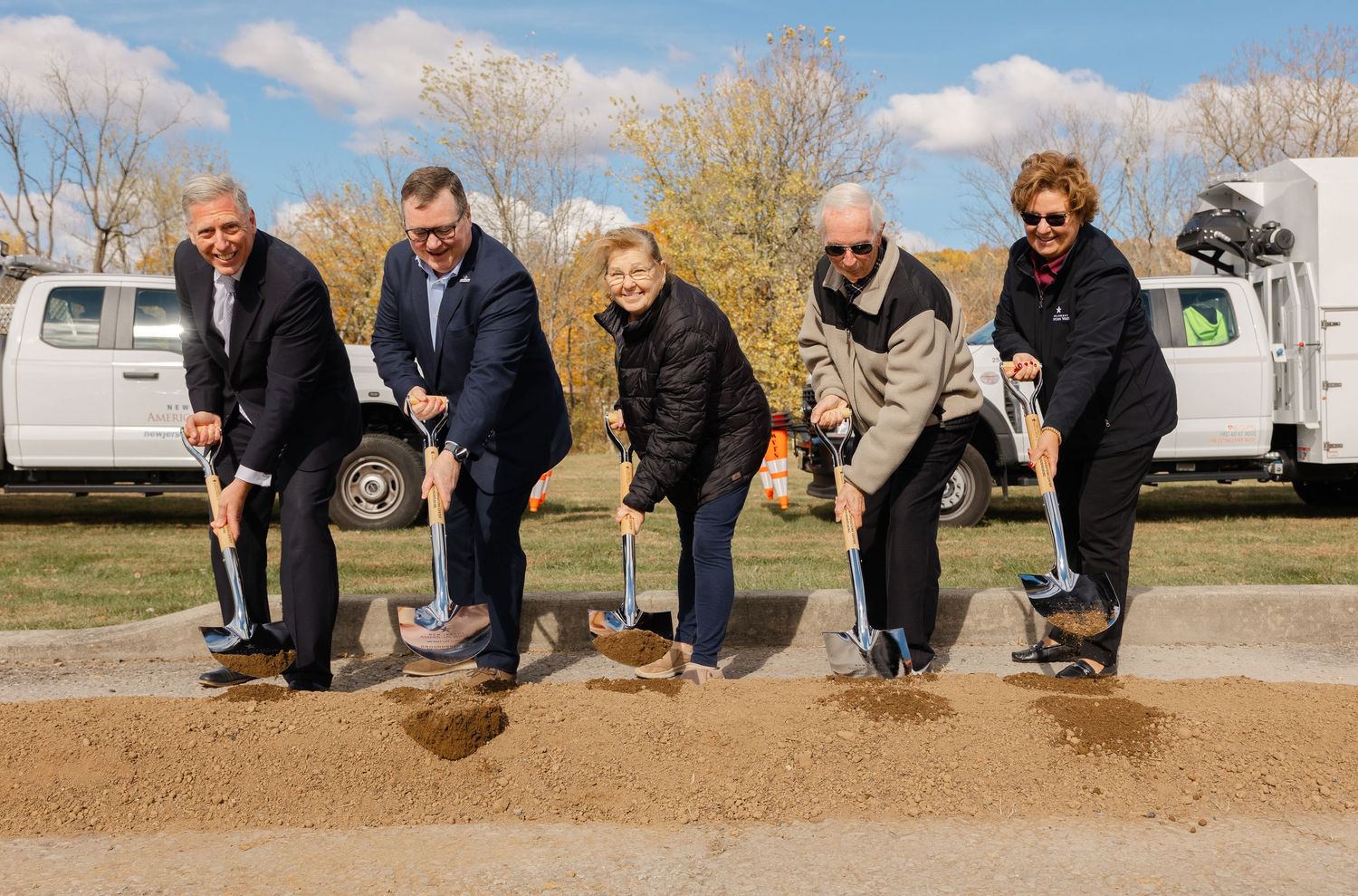 Line of people kneeling on dirt ground during an outdoor ceremony.