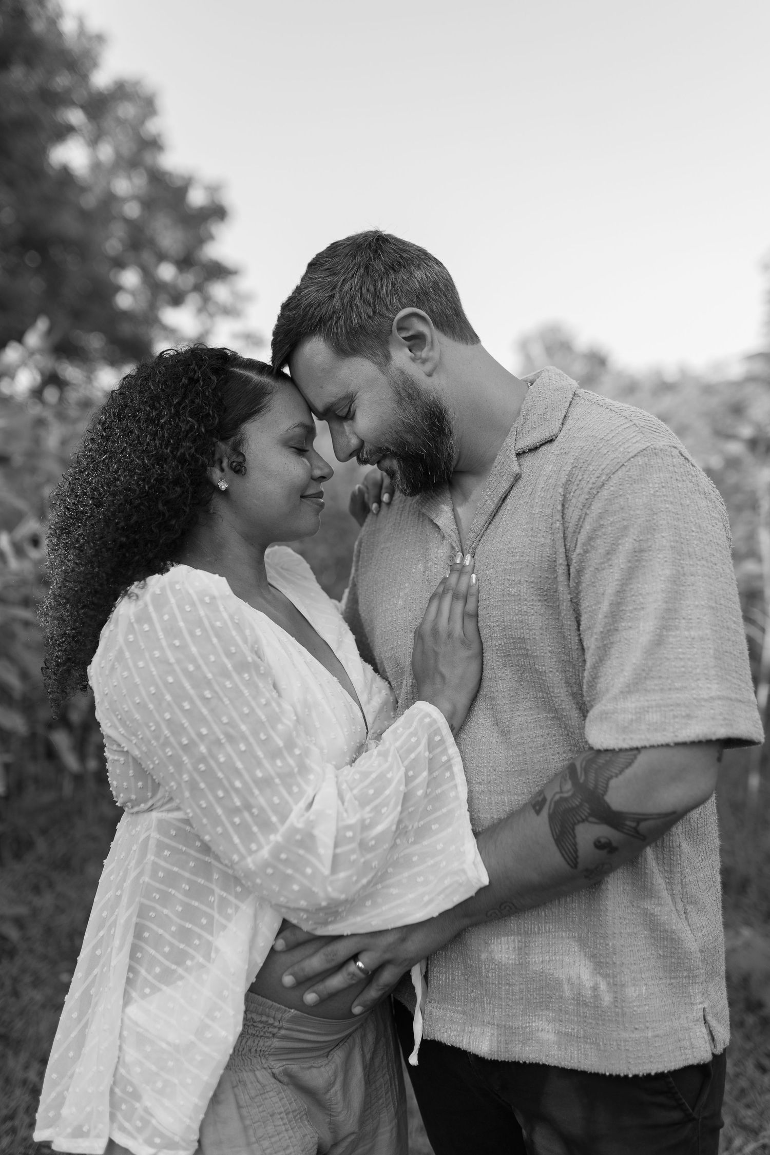 Black and white photo of a couple sharing an intimate forehead touch moment outdoors surrounded by greenery.