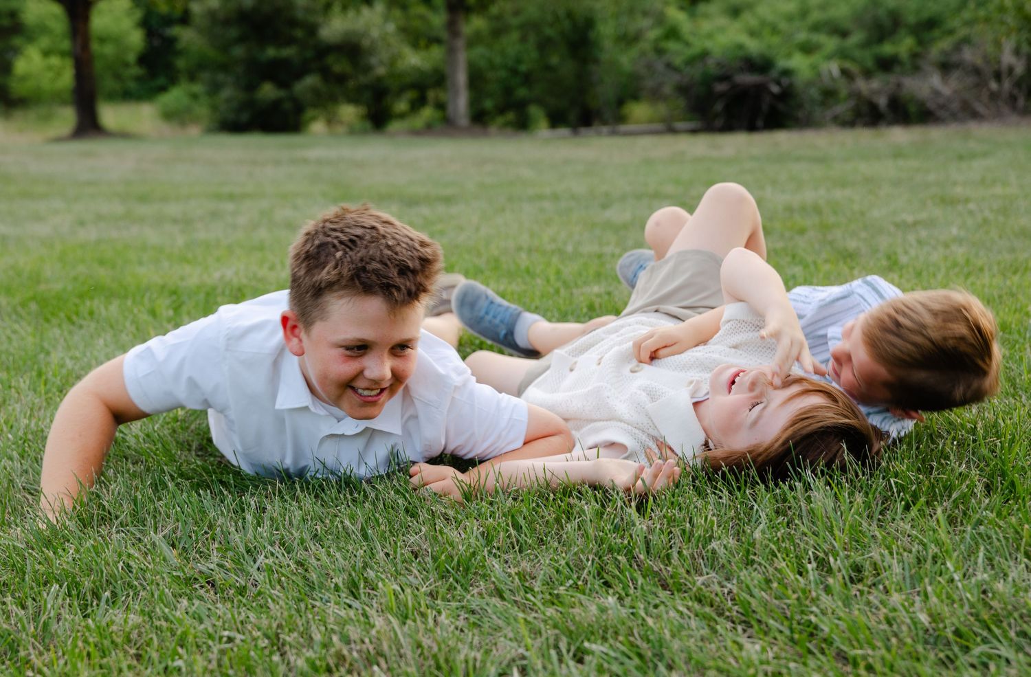 Two children laugh and play together while lying on lush green grass outdoors.