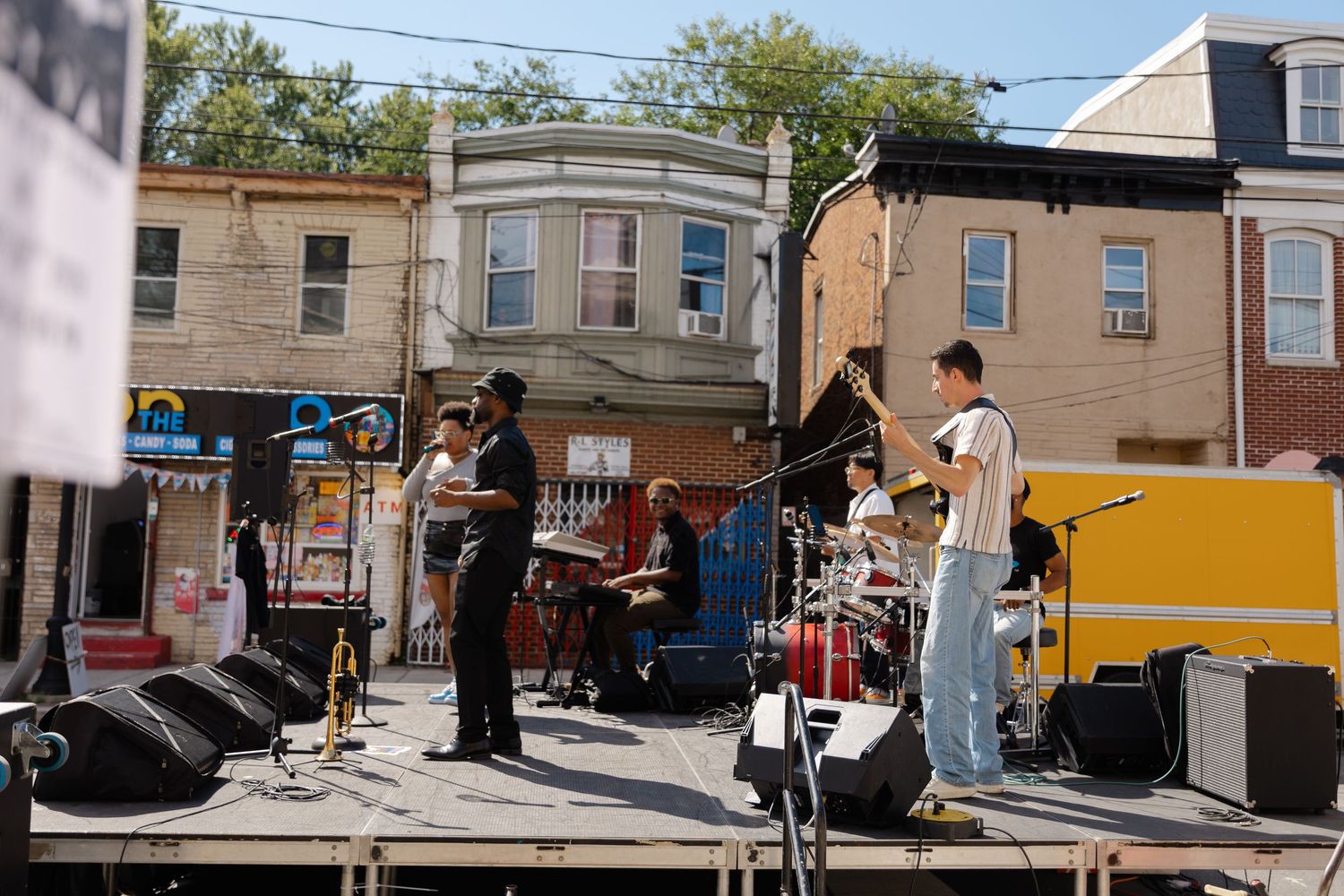 Live band performing on an outdoor stage at a street festival with urban row houses in the background.