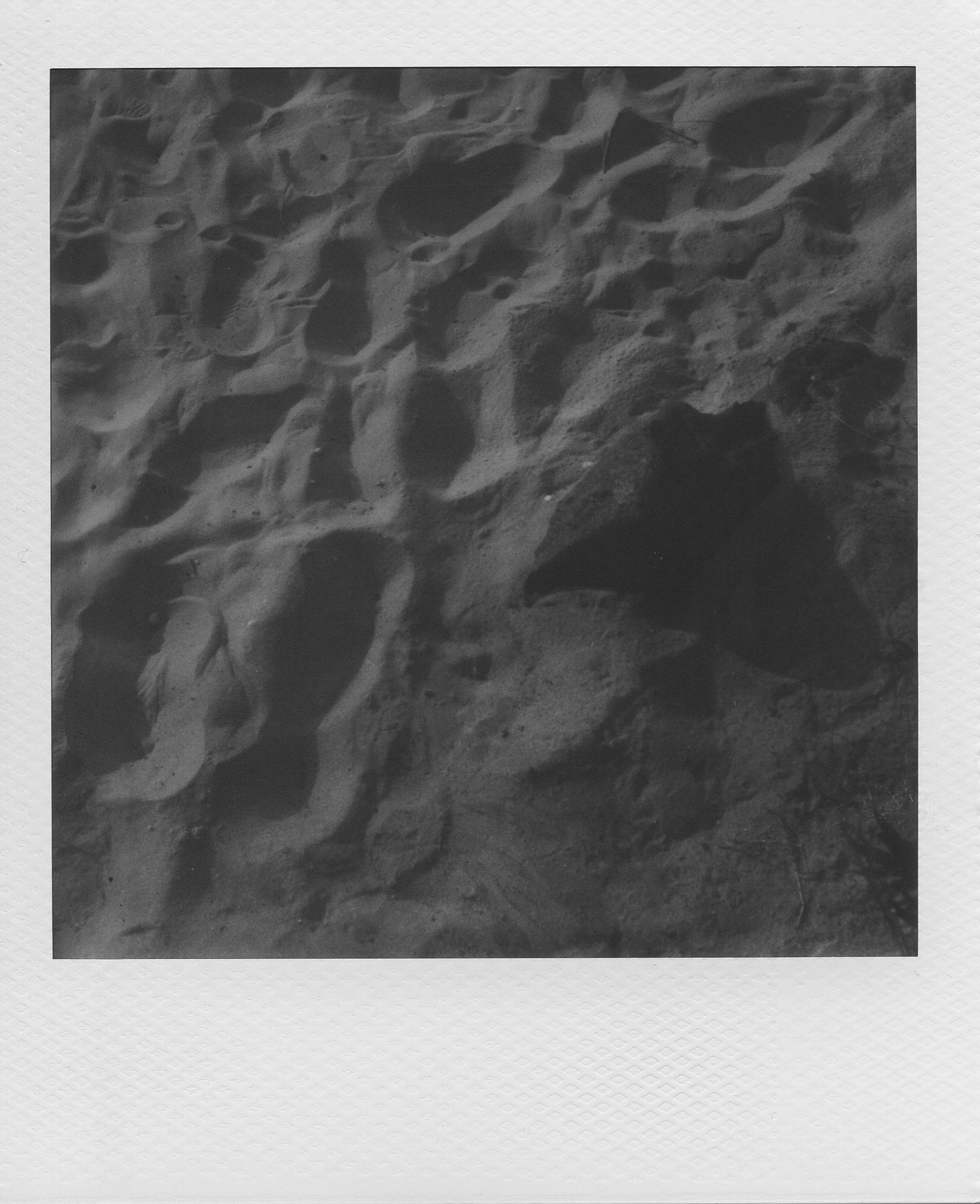 Close-up black and white polaroid photo of rugged lunar-like rocky terrain with deep shadows and craters.