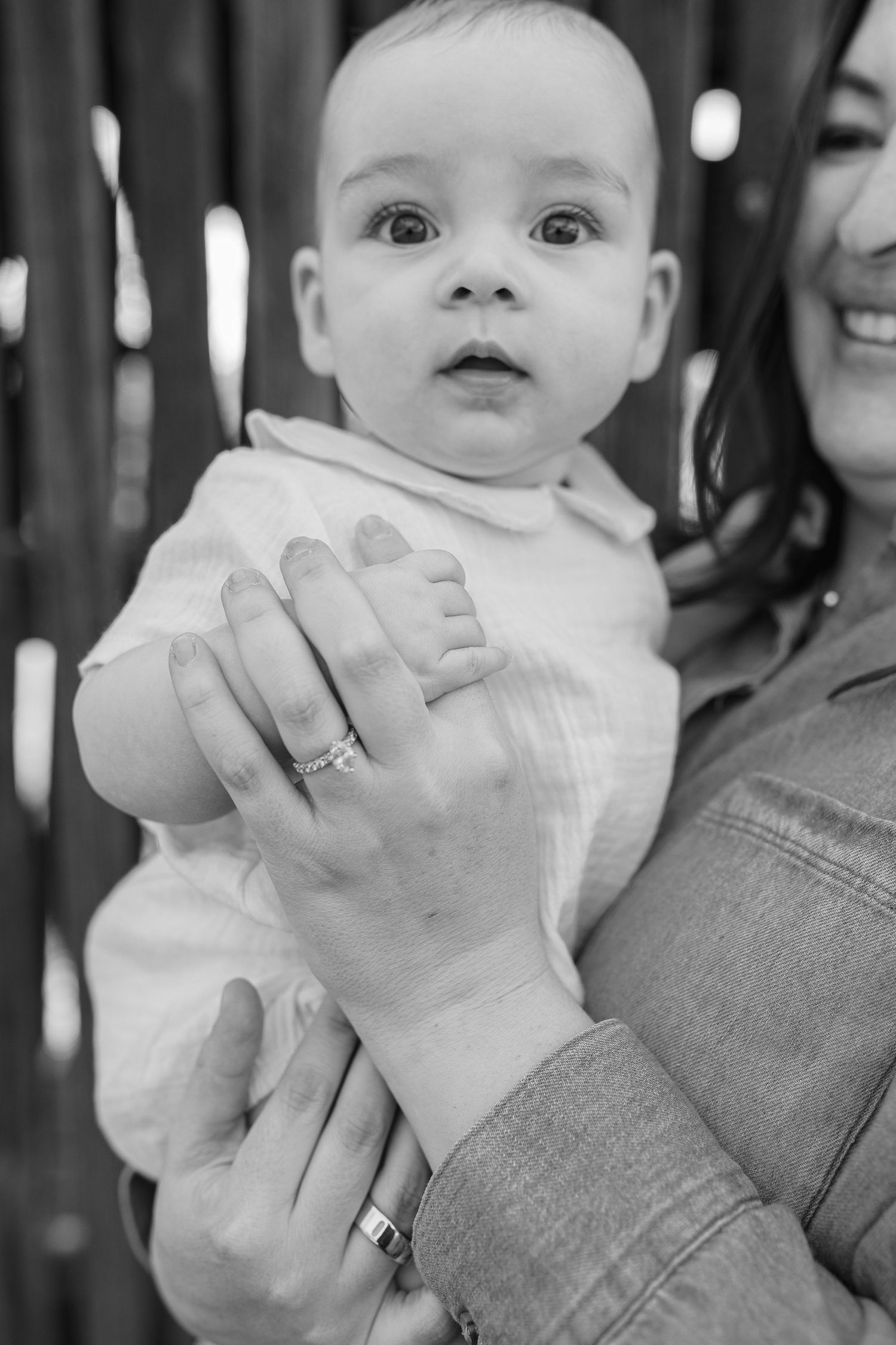 Black and white close-up of a wide-eyed baby being held by a mother wearing rings and bracelet.