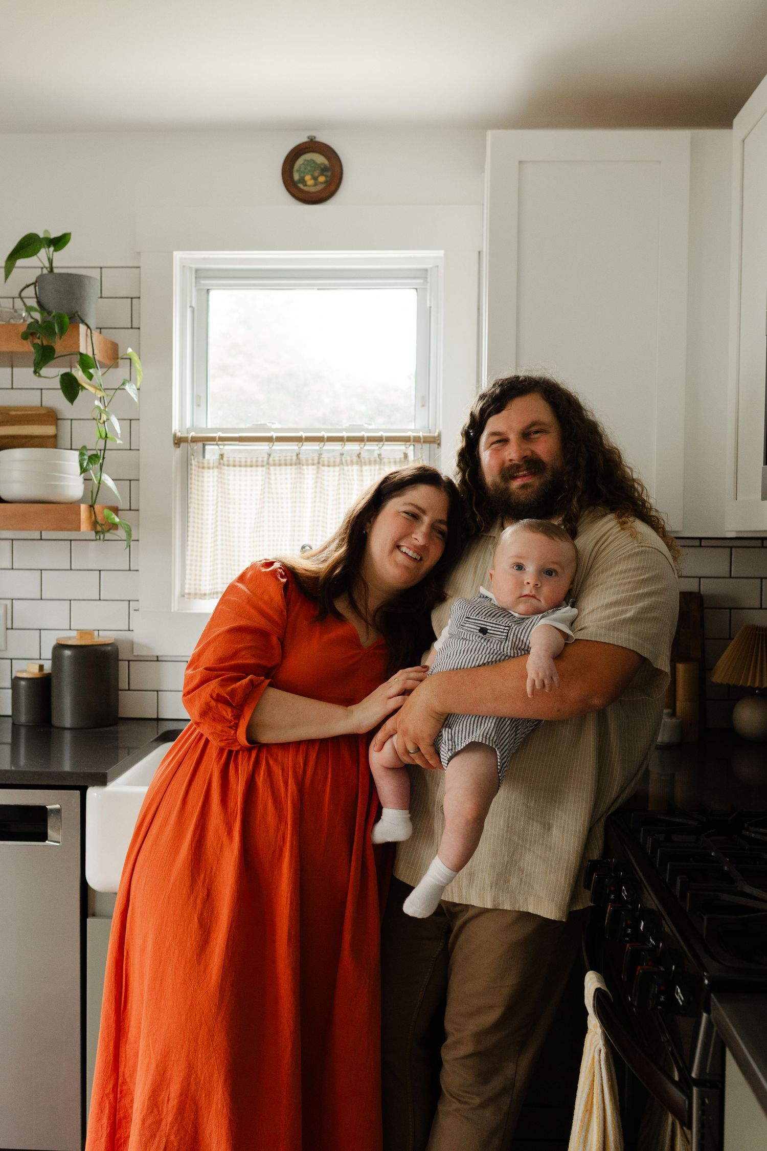 Smiling couple in a modern kitchen holding their baby, posing together for a family portrait.