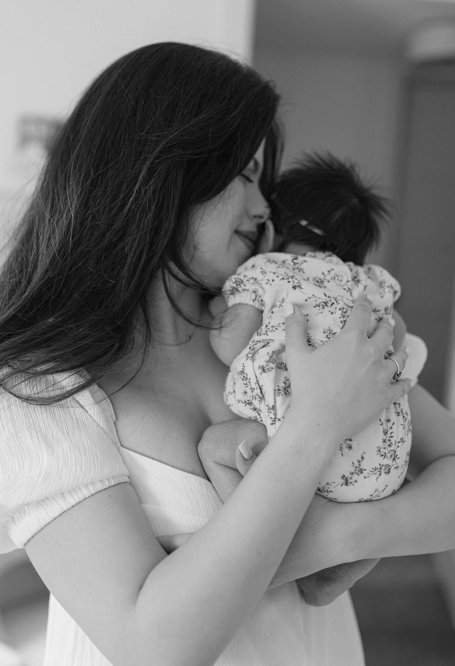 A mother with long dark hair gently holds her newborn baby in a black and white photo.