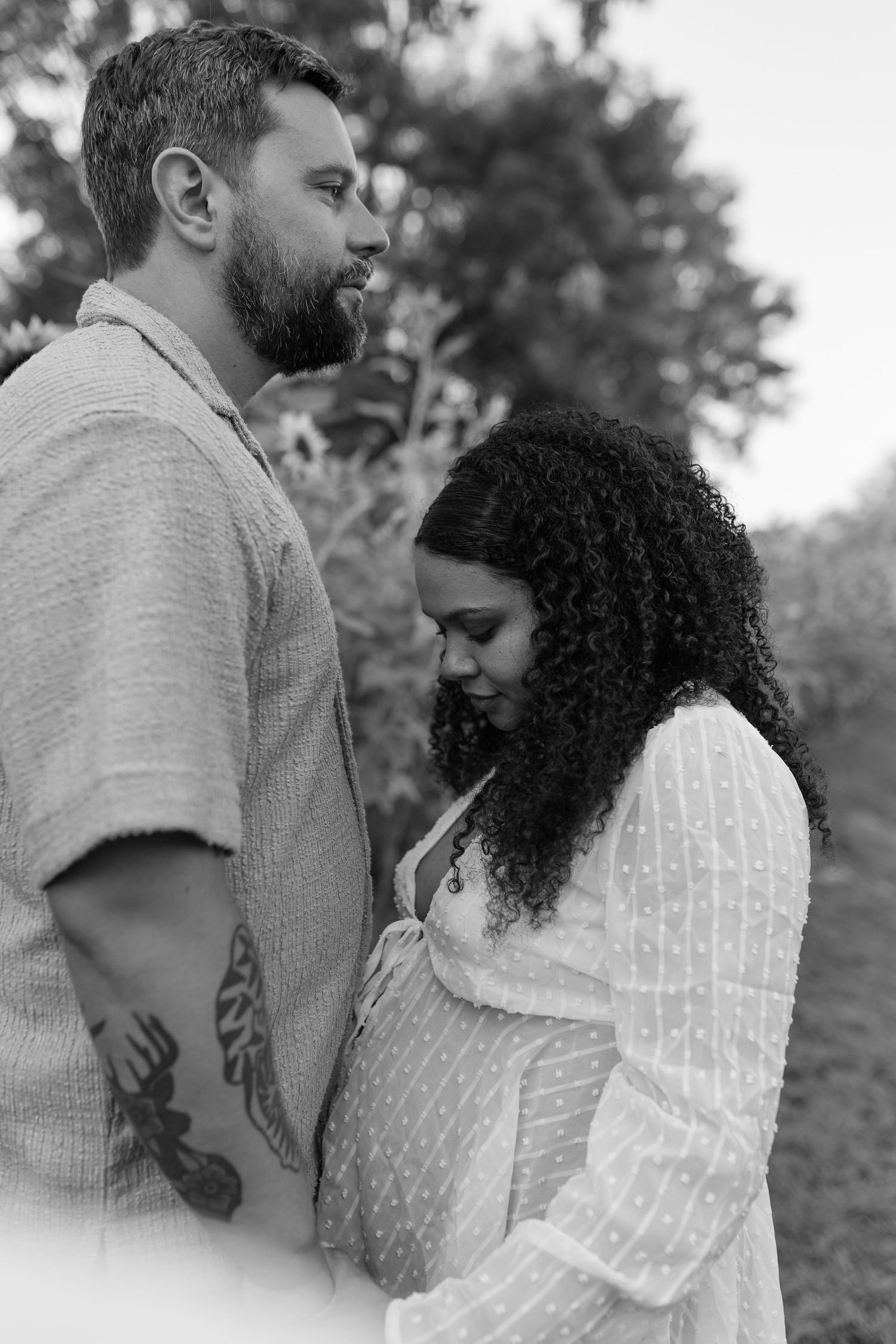 Black and white maternity photo of a couple standing close together, woman cradling her pregnant belly.