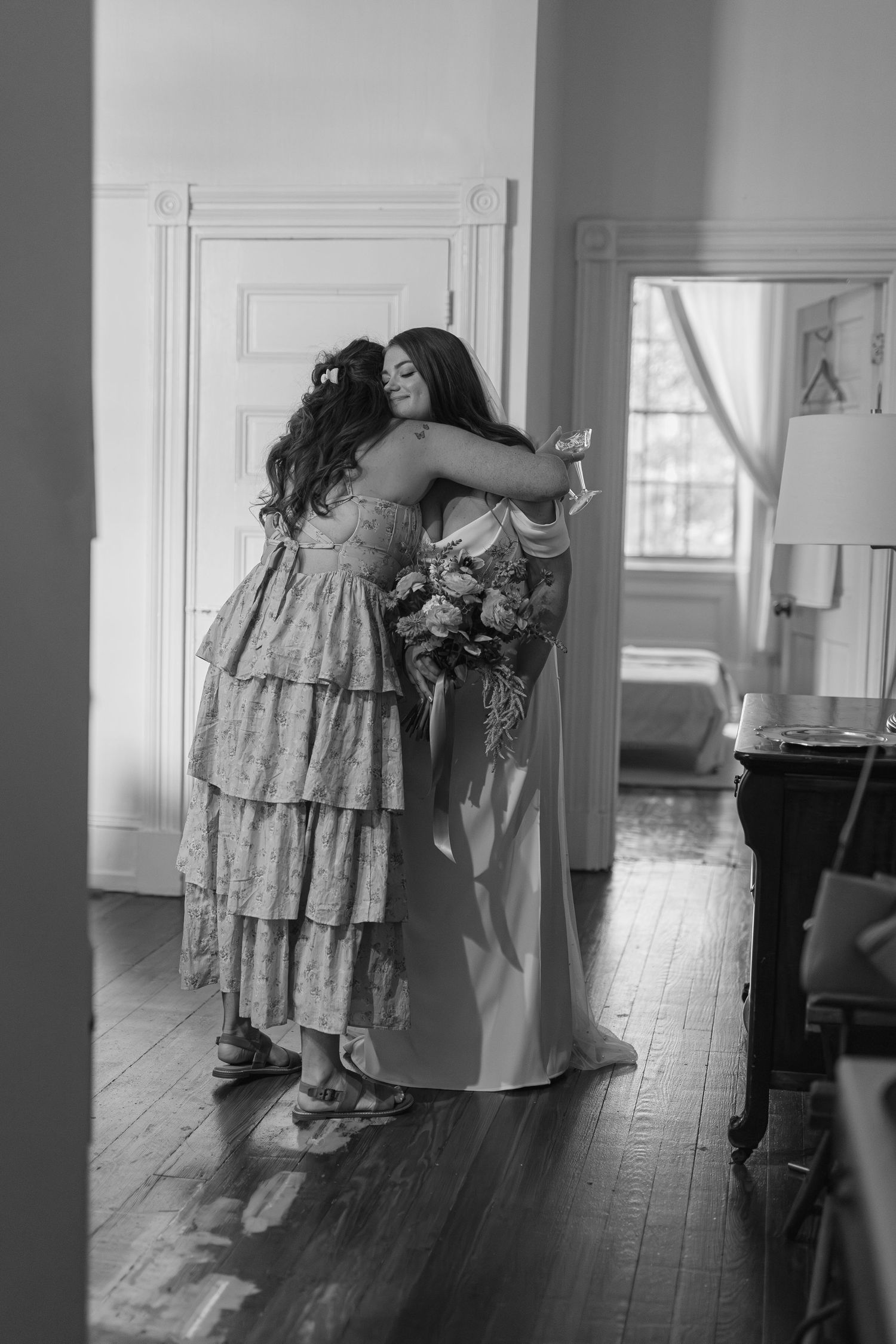 Black and white photo of a bride and bridesmaid sharing a heartfelt hug before the wedding ceremony.
