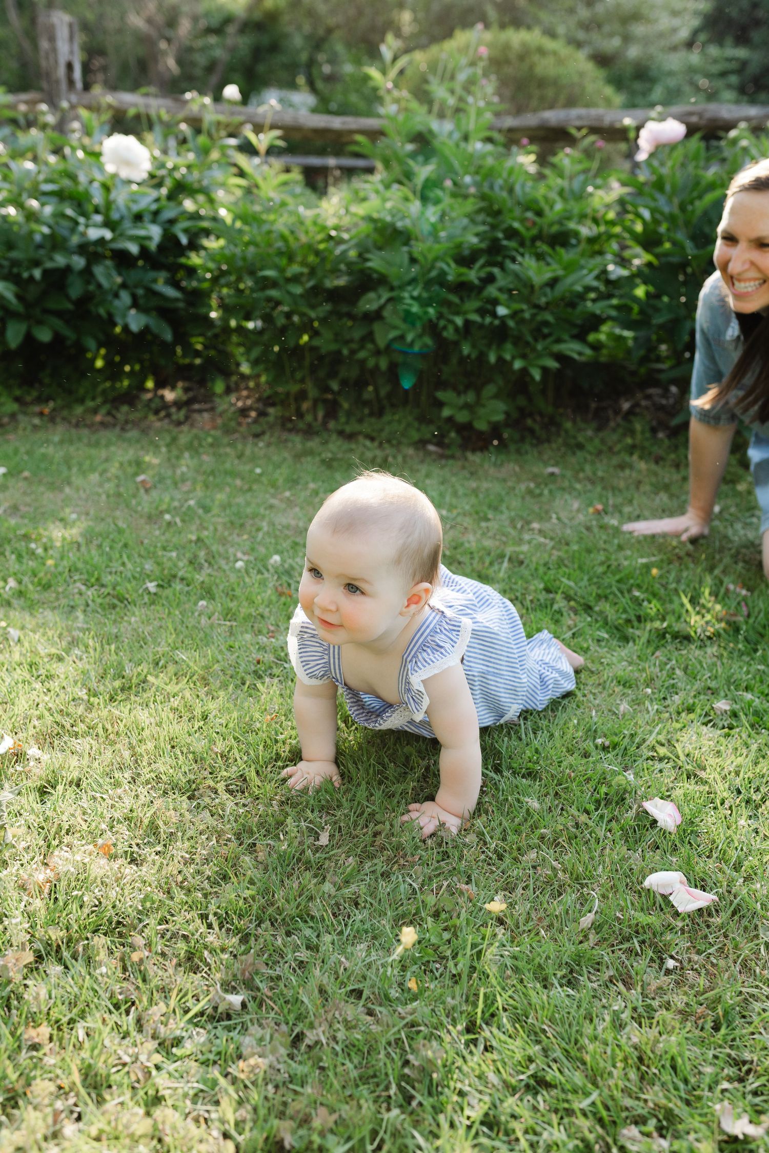 Curious baby in striped romper crawling on green grass in a sunny garden setting.