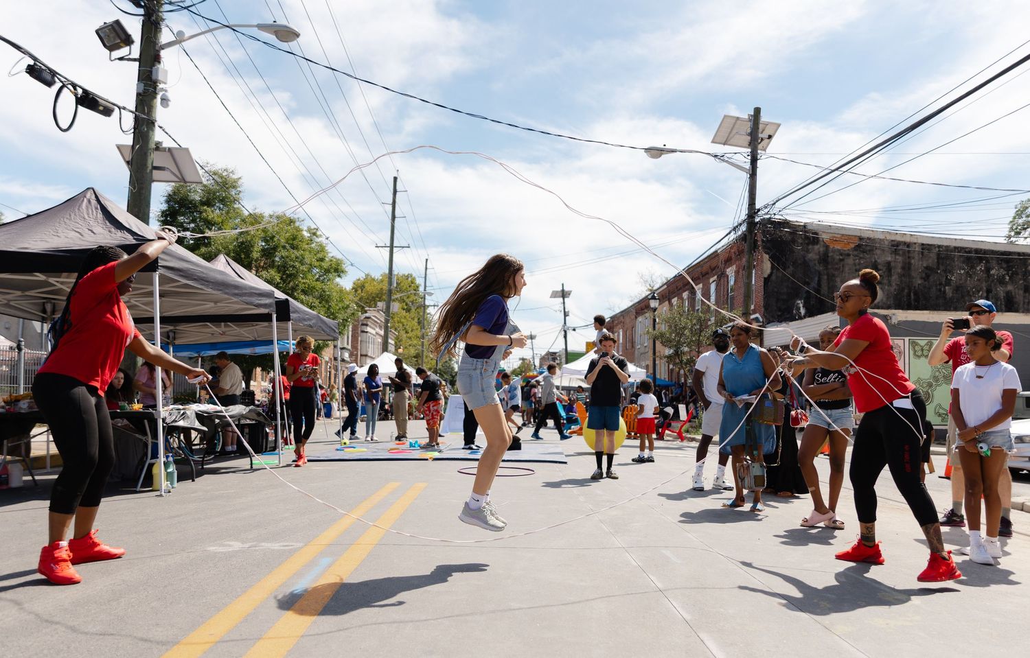 Children jump rope on a closed street during an outdoor community festival on a sunny day.