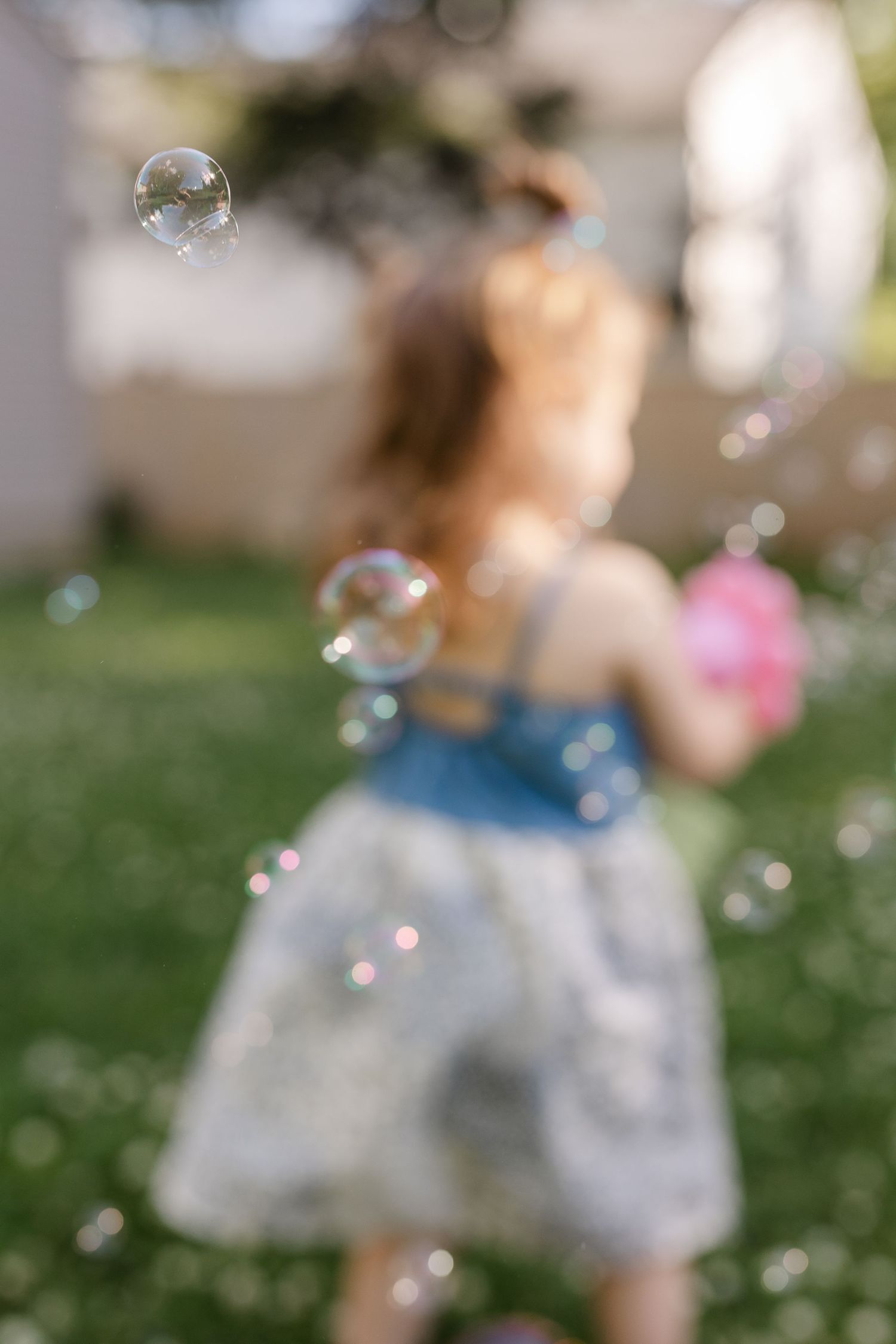 Blurred artistic shot of a young girl chasing soap bubbles in a sunny green backyard.